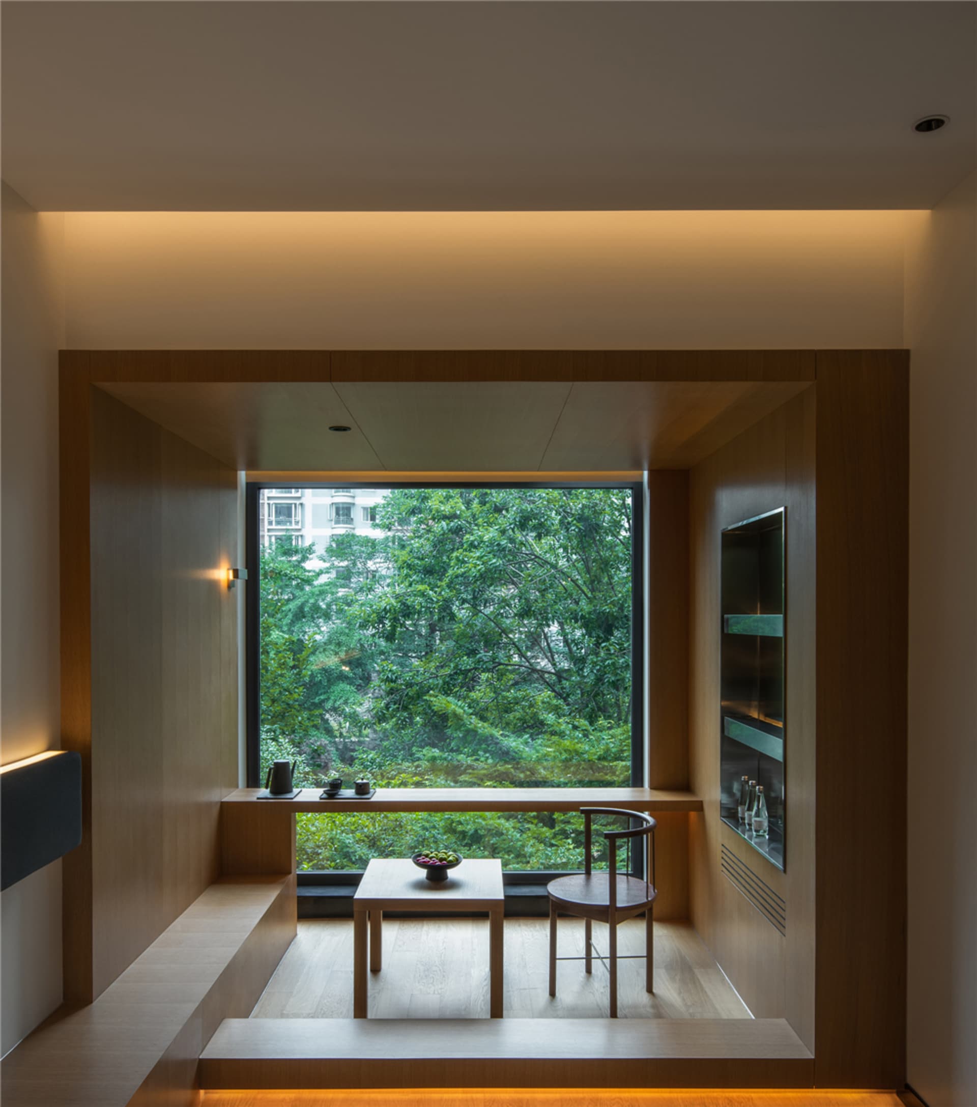 Modern living room with wooden furniture and large window overlooking greenery.