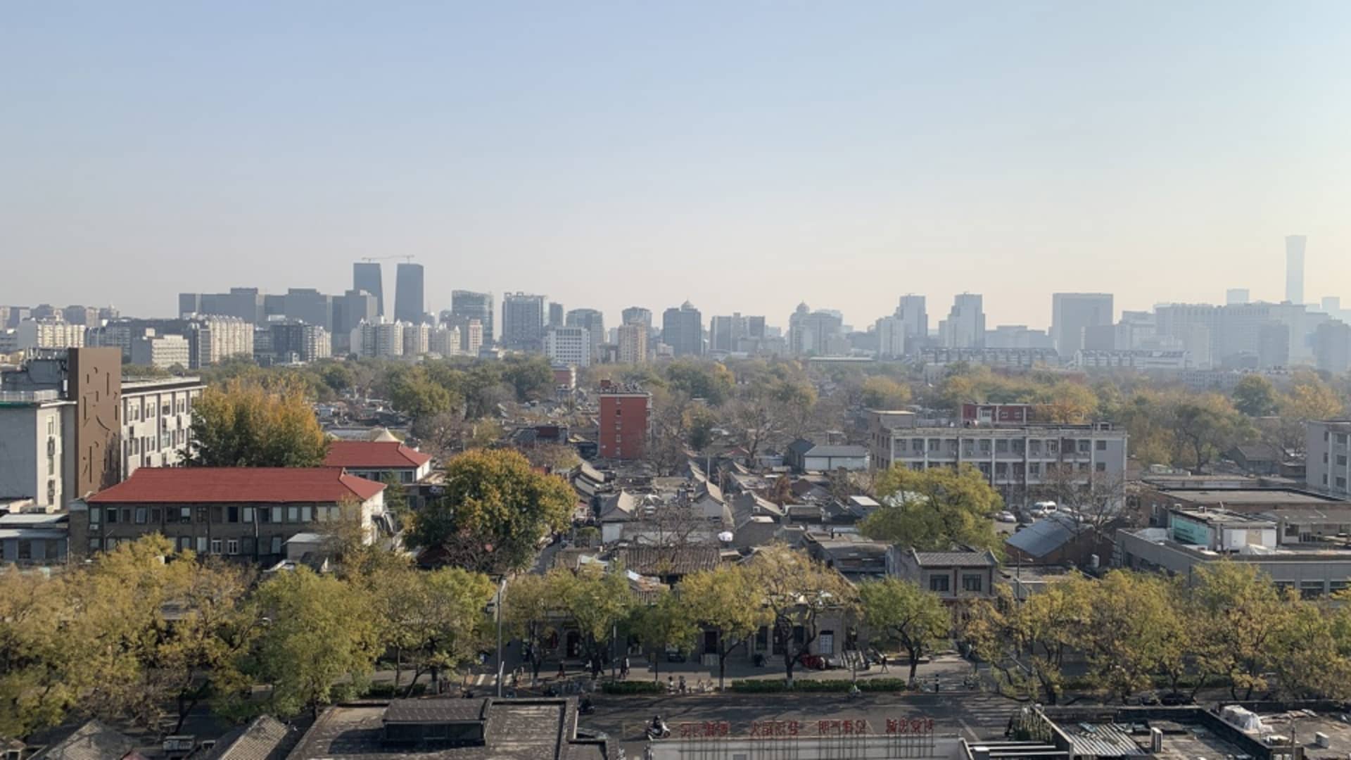 都市街景，前景有建築物與樹木，遠處是現代摩天大樓。