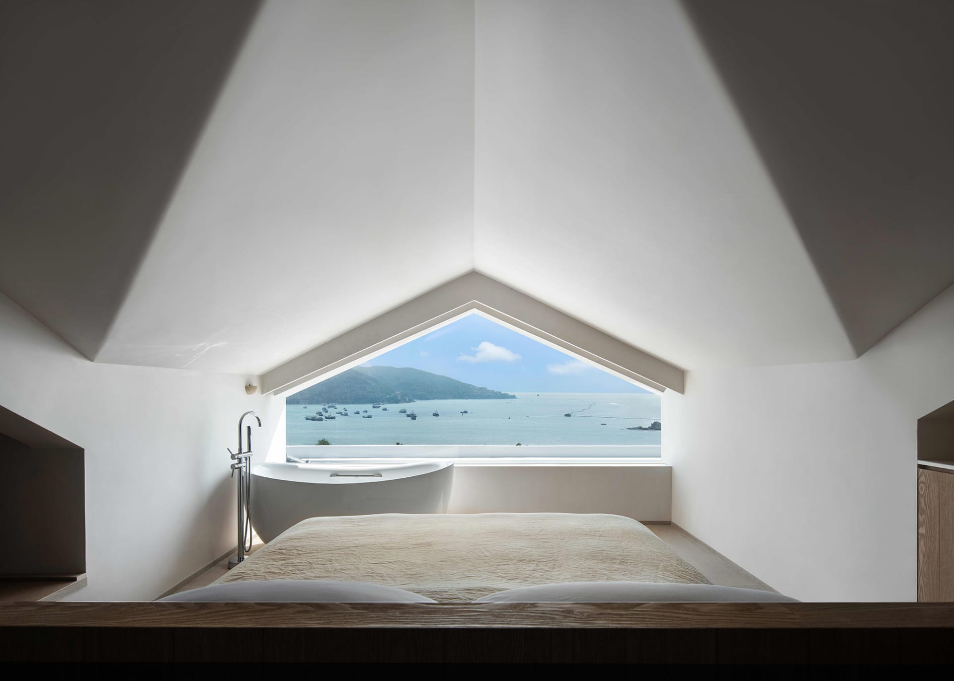 A modern minimalist bedroom with concrete walls featuring a large window overlooking the ocean.