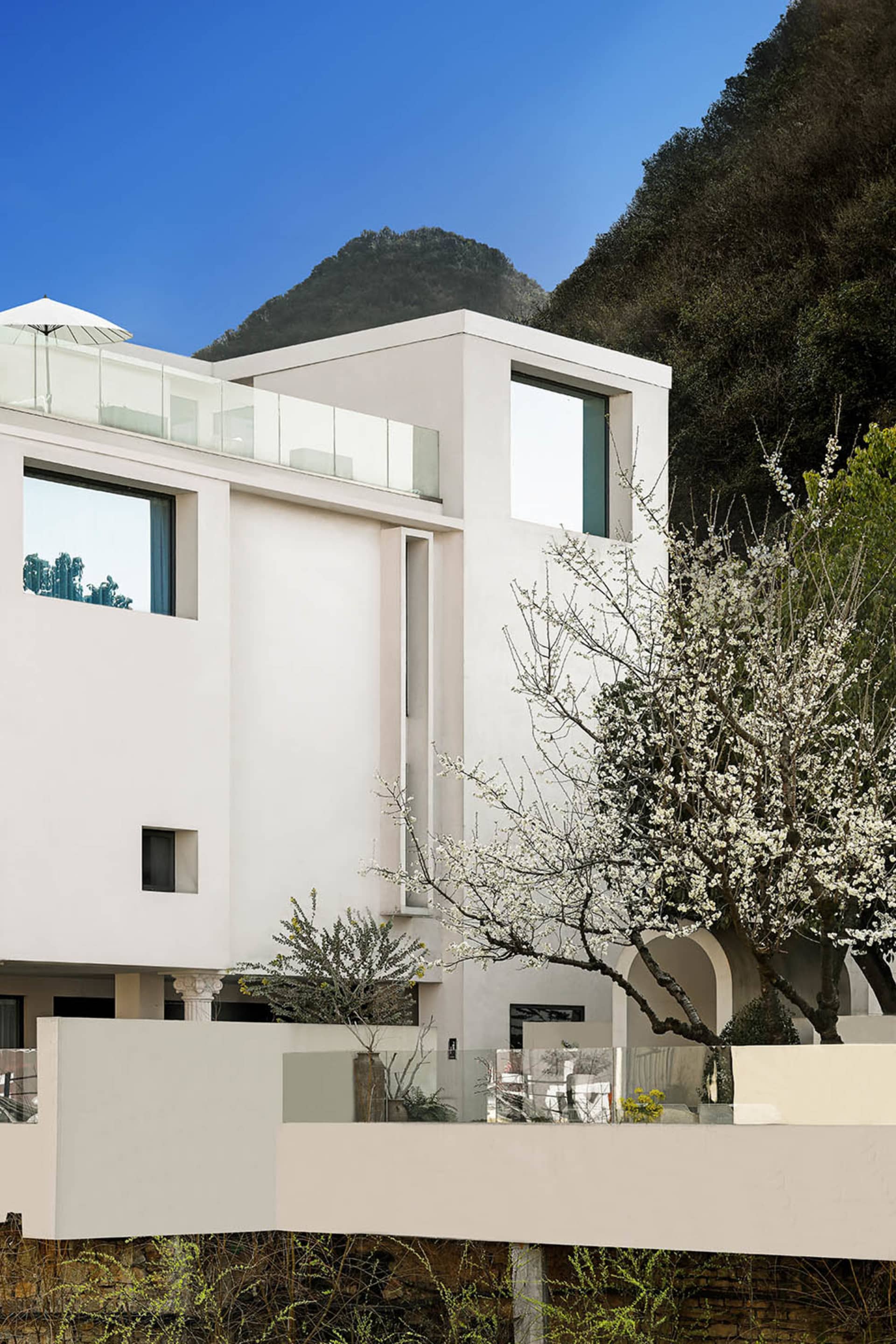 A modern residential building with a minimalist design, featuring concrete and glass materials, set against a mountainous bac
