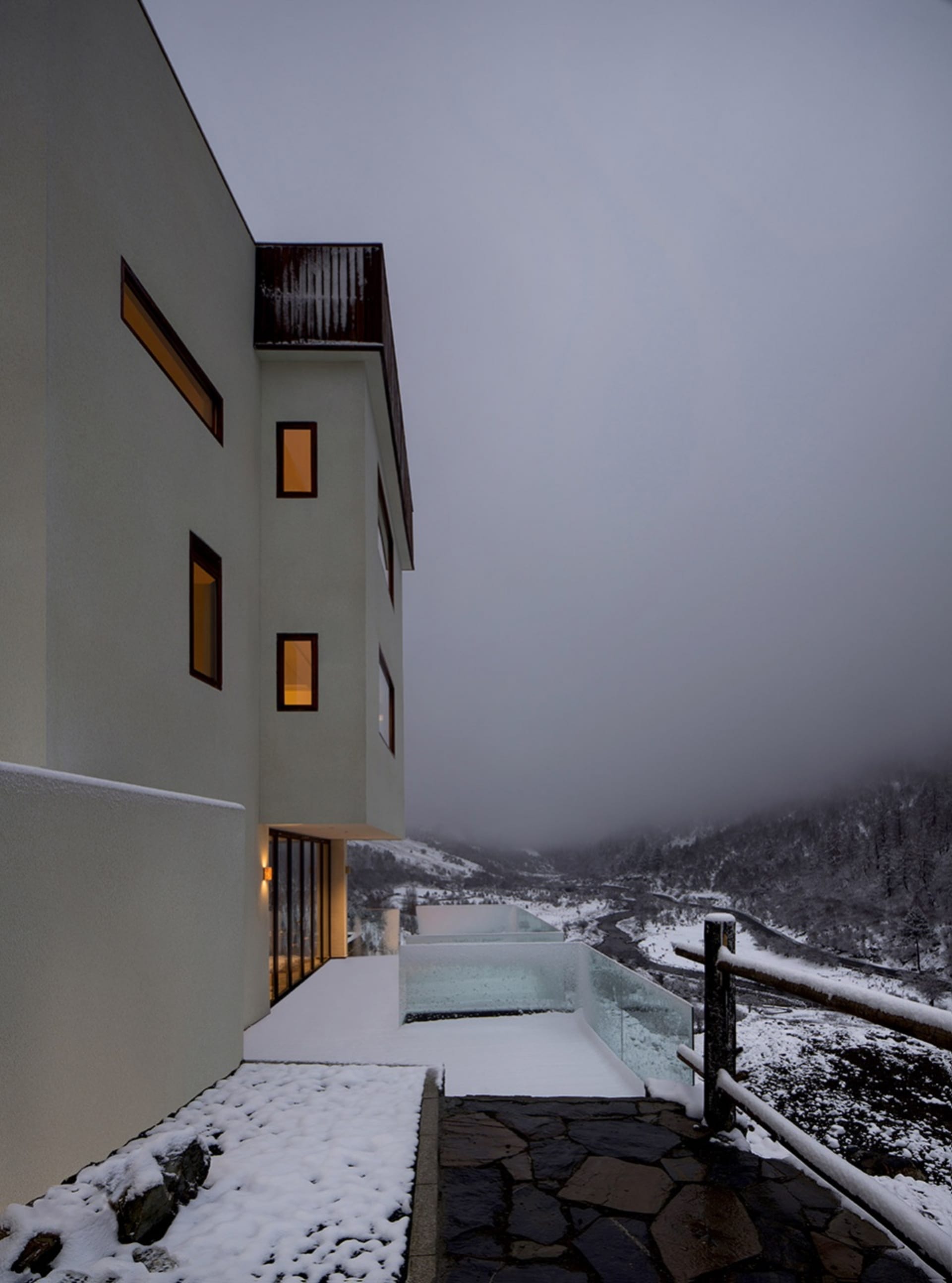 Modern residential building with white exterior and snow-covered roof and landscape.