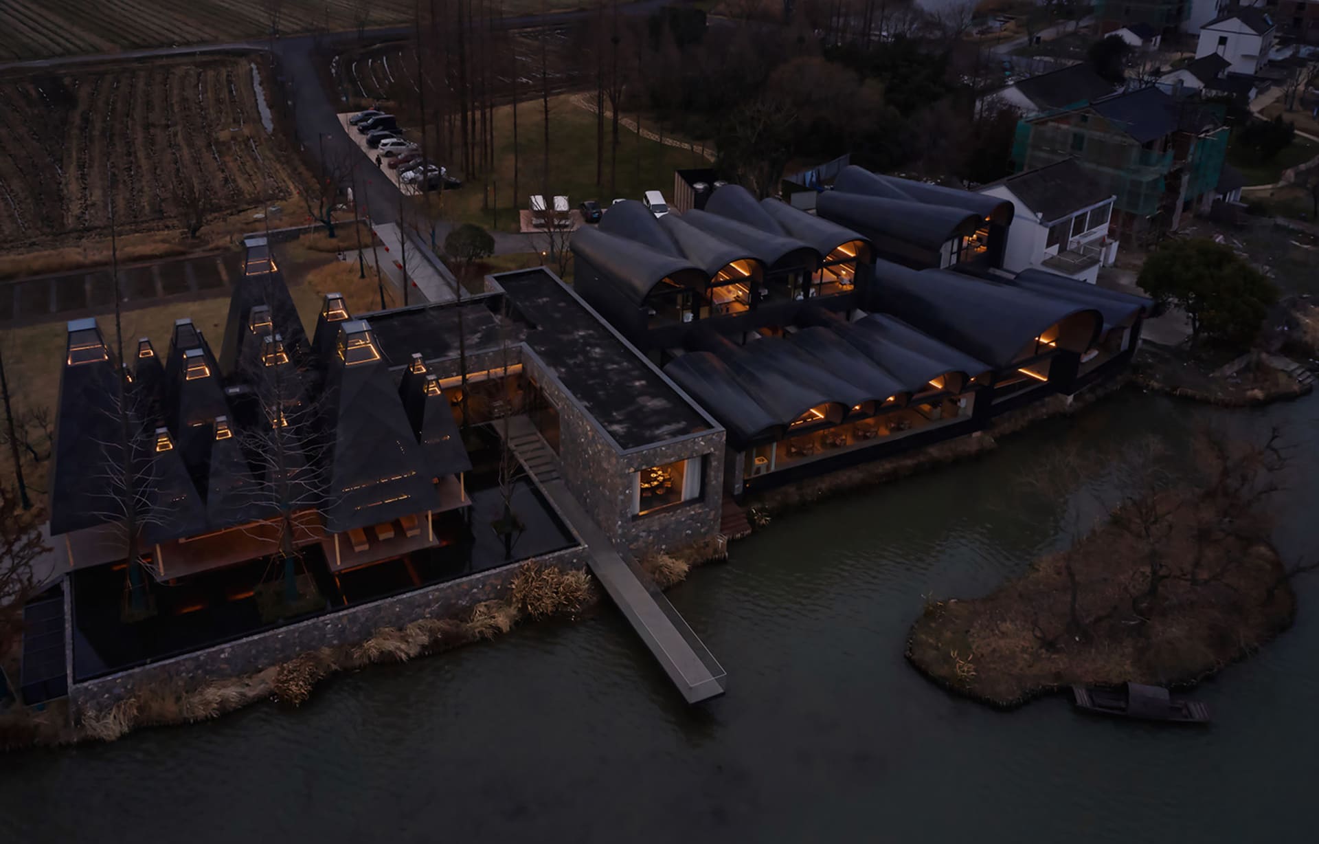 A modern residential space featuring glass roofs and gray-tiled facades surrounded by a water body, with a parking area and t