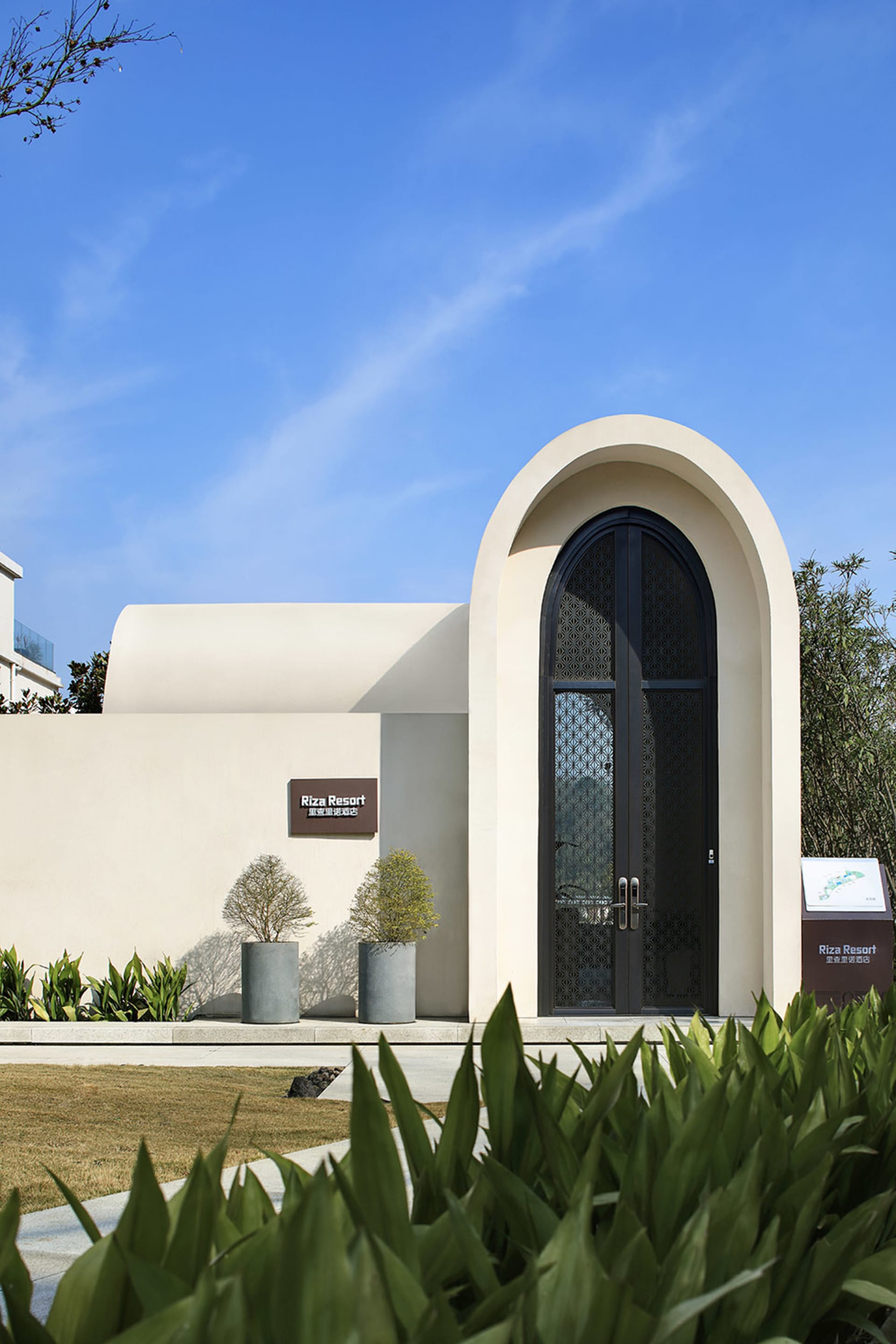 A modern cement entrance featuring an arched door and minimalist design, part of a resort.