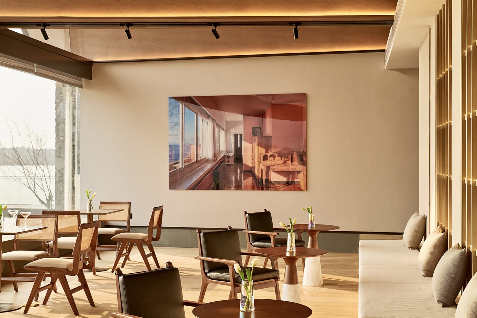 Modern restaurant bar interior with wooden furniture, tables, and chairs, featuring a large framed photograph on the wall.