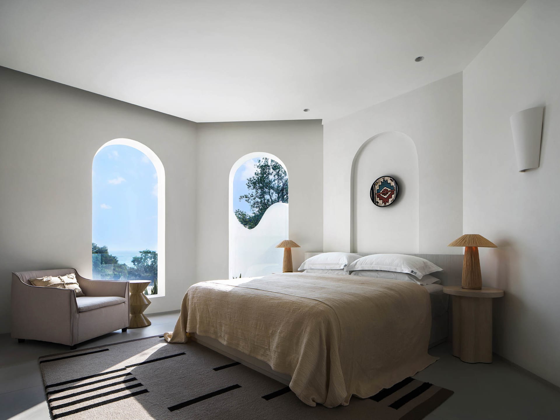 A modern bedroom with white walls, a large bed, and arched windows.