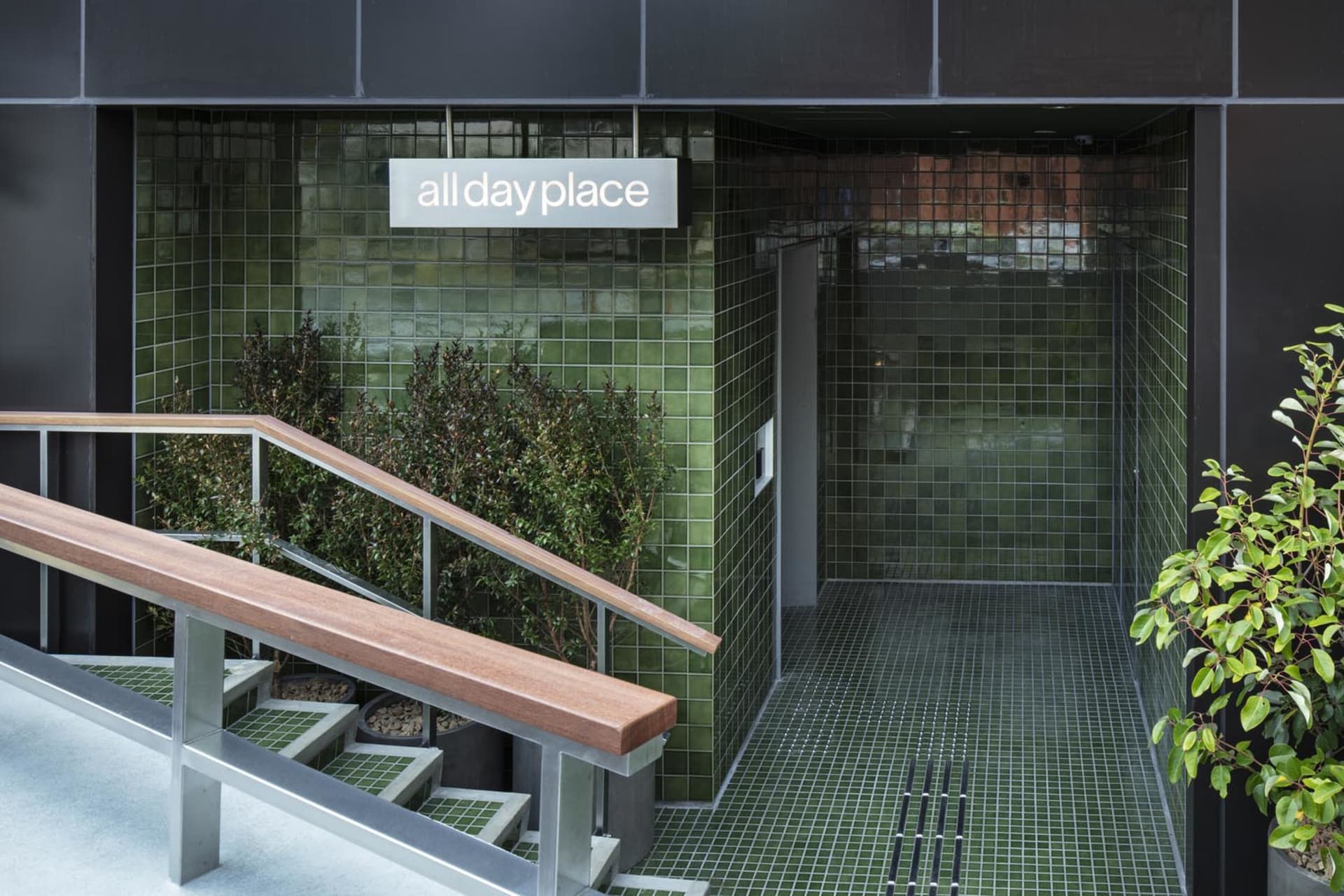 An entrance to a commercial building with green tiles and a handrail.