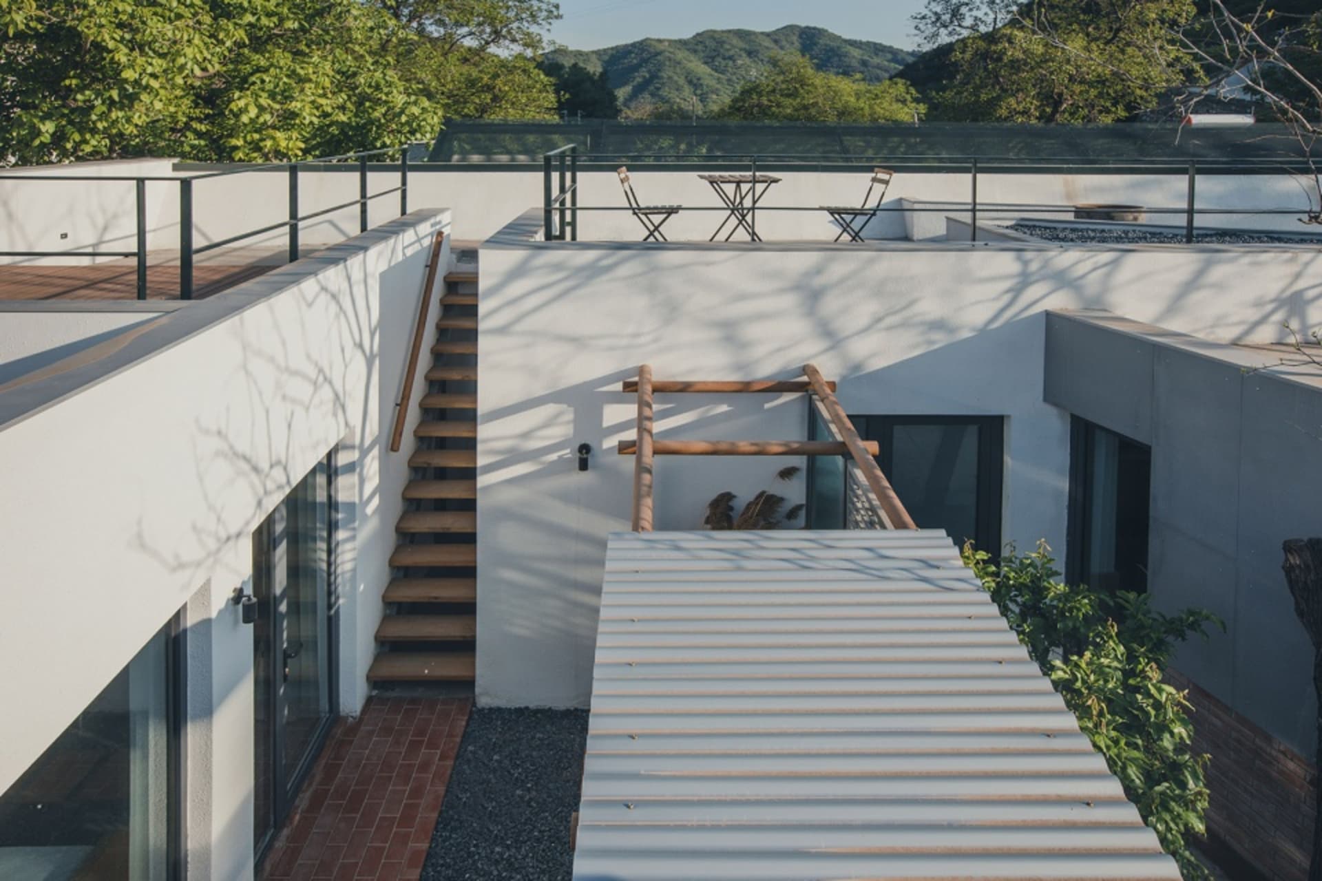 A minimalist house with a metal roof surrounded by trees and mountains.