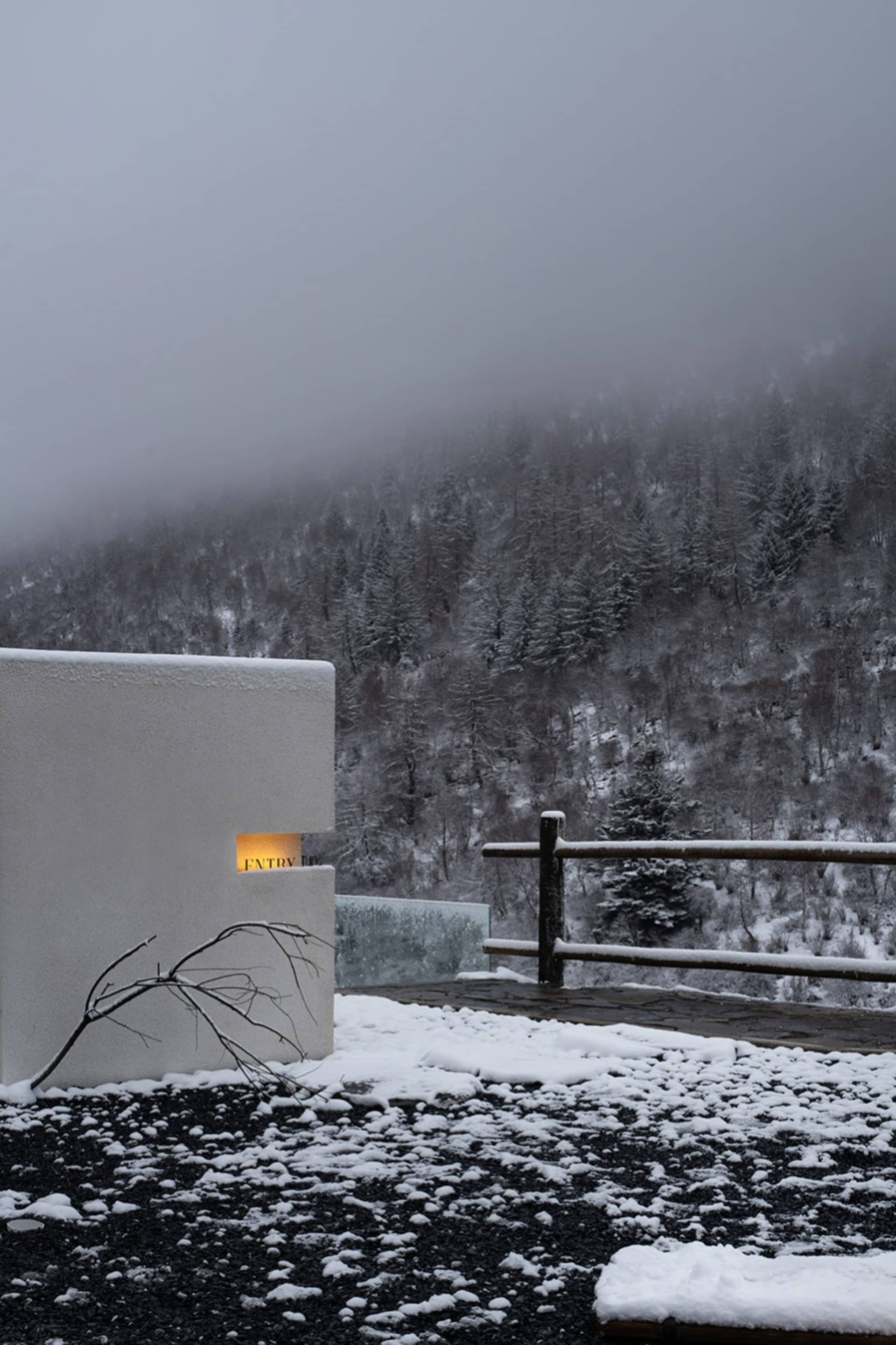A minimalist white structure surrounded by a snowy landscape with a wooden fence.