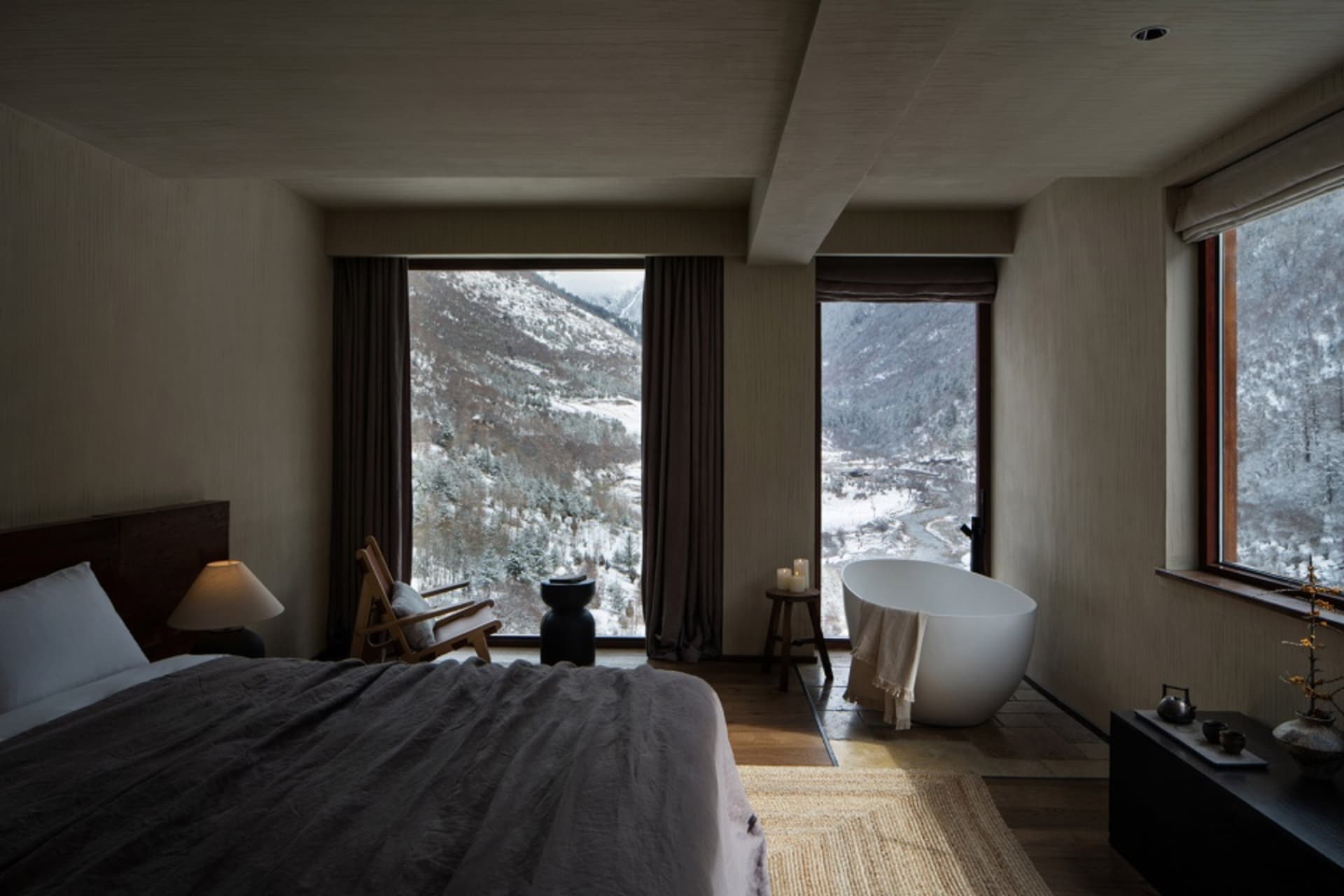 A modern bedroom featuring a carpeted floor, minimalistic furniture, and a view of snowy mountains through large windows.