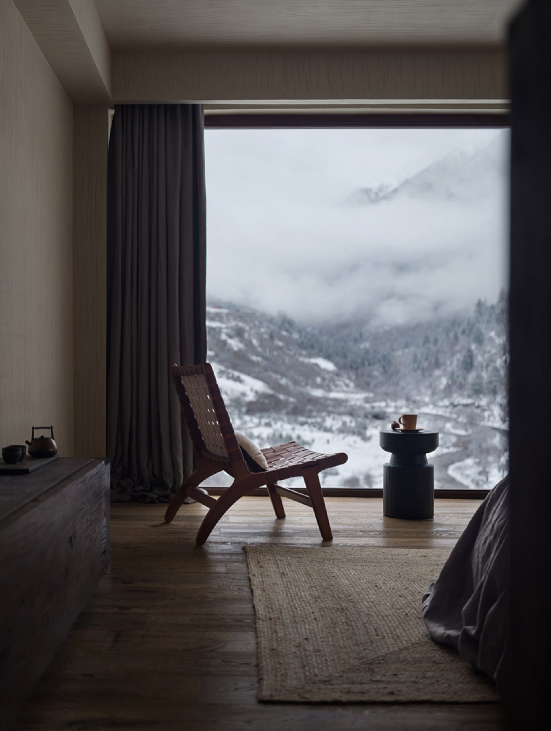 A bedroom with a mountain view, featuring a wooden chair and a side table with a cup and saucer.