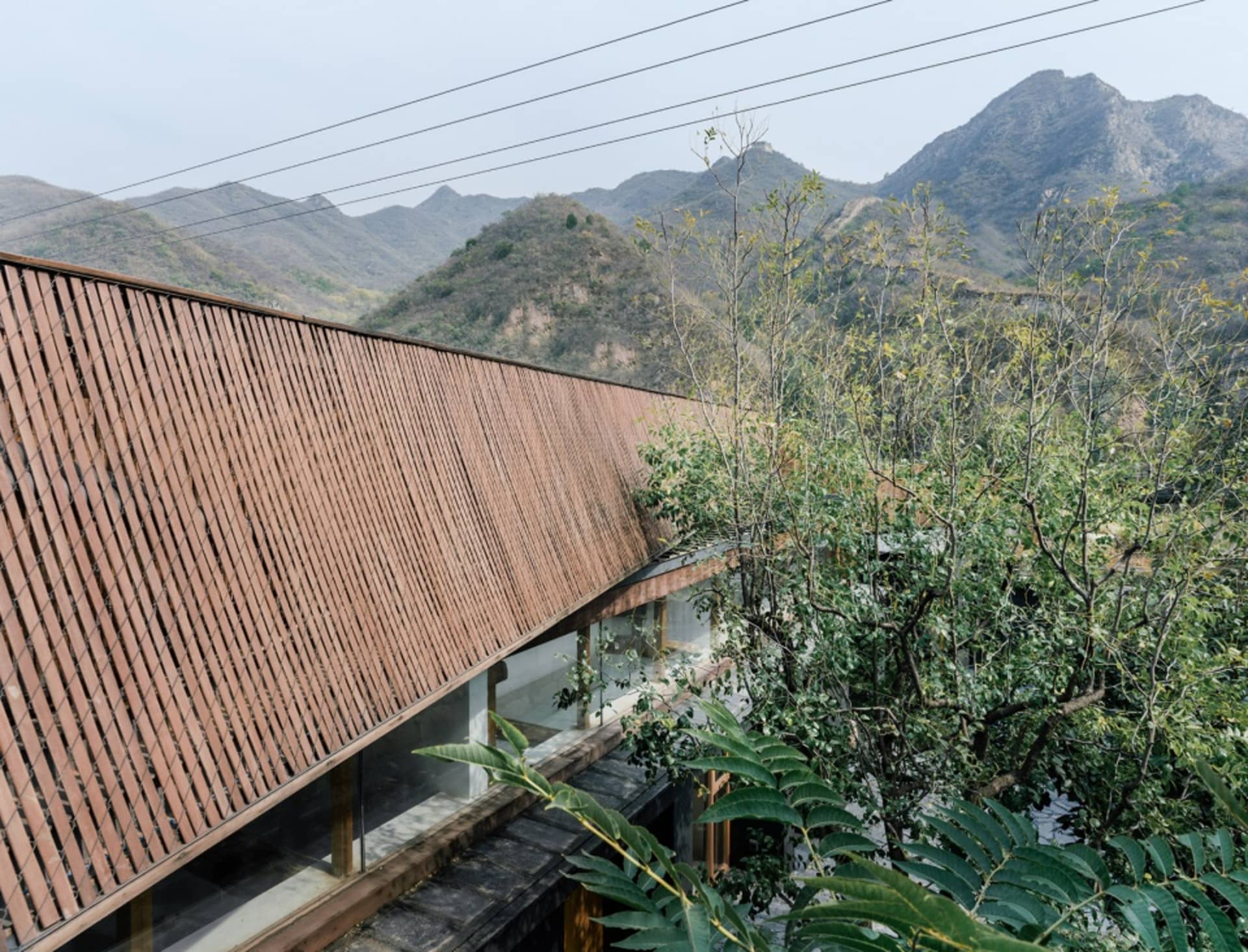 現代建築外觀，搭配木條屋頂與玻璃牆，背景為綠意與山景環繞