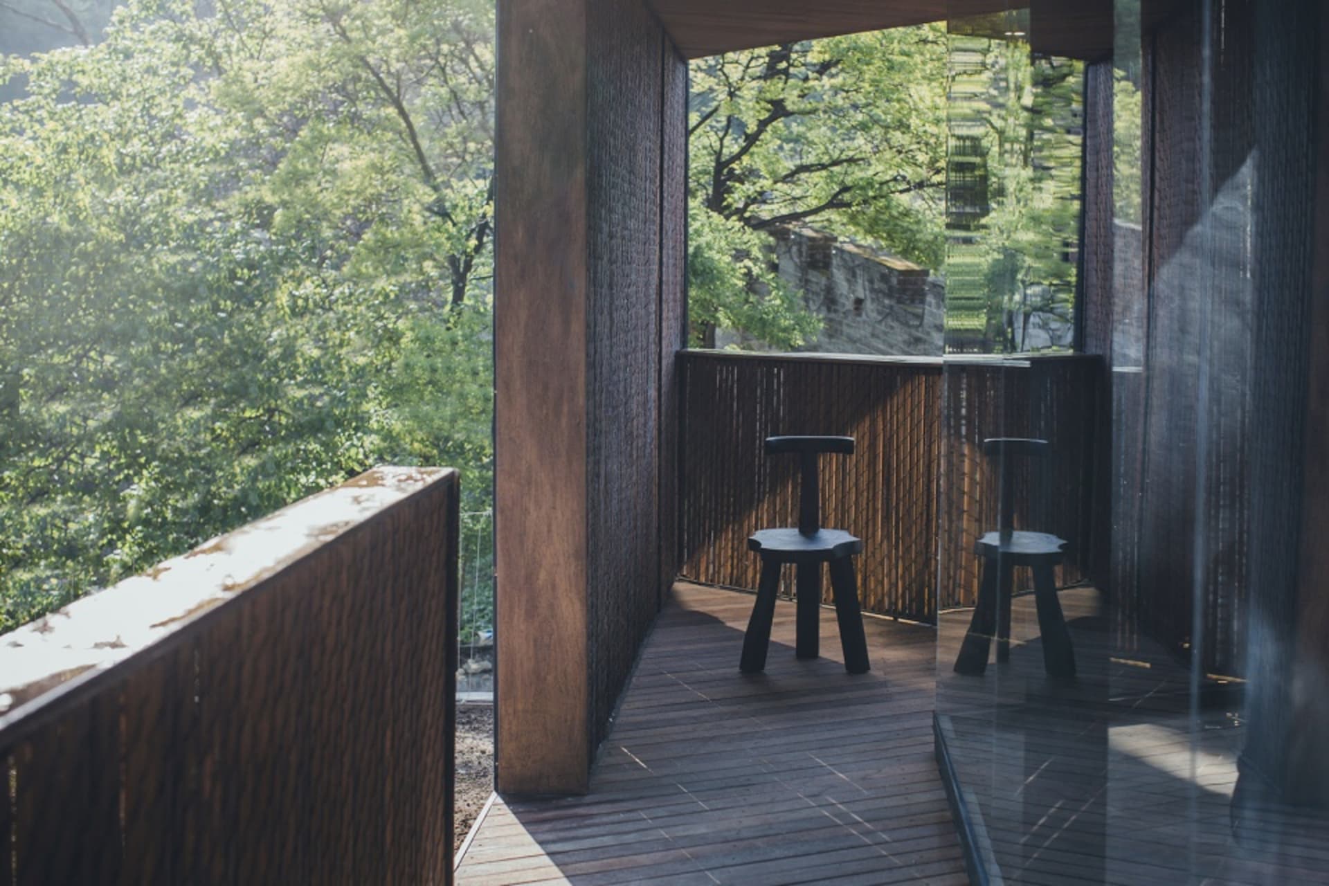 A modern outdoor wooden balcony with greenery in the background.
