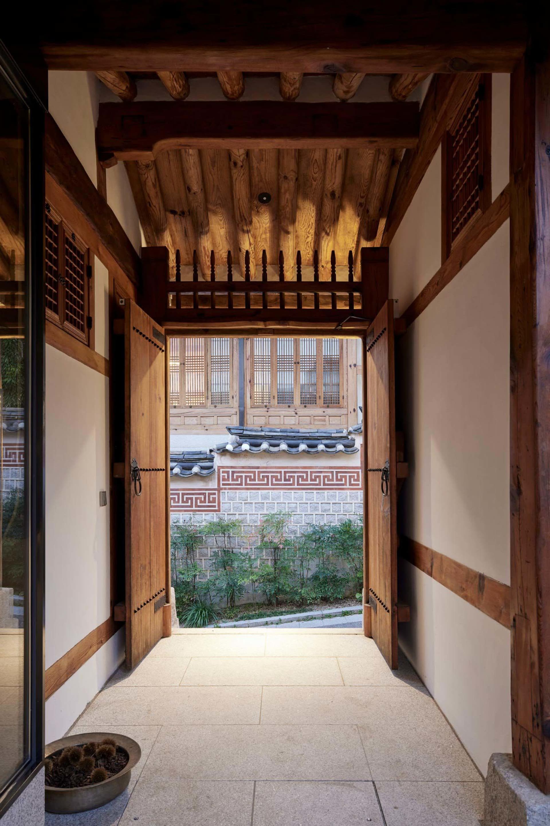傳統木製門廊通往石板庭院，四周環繞韓式建築元素。