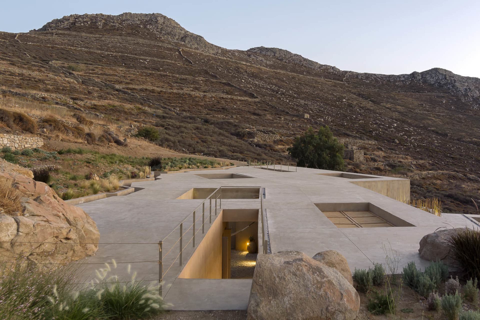 Modern minimalist cement home surrounded by rocky terrain and hills.