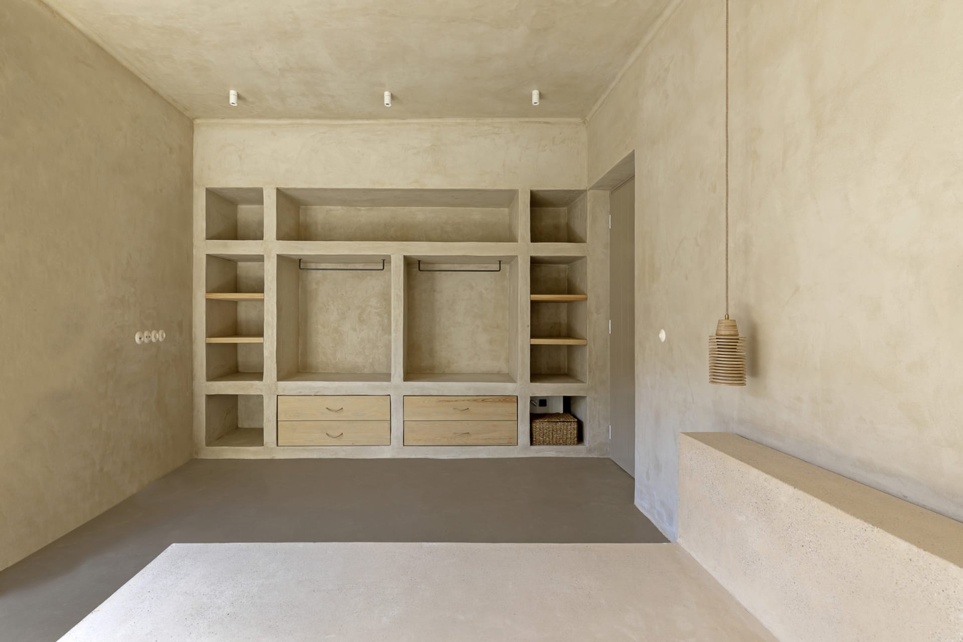 A minimalist closet with concrete walls and floor, featuring built-in shelves and wooden drawers.