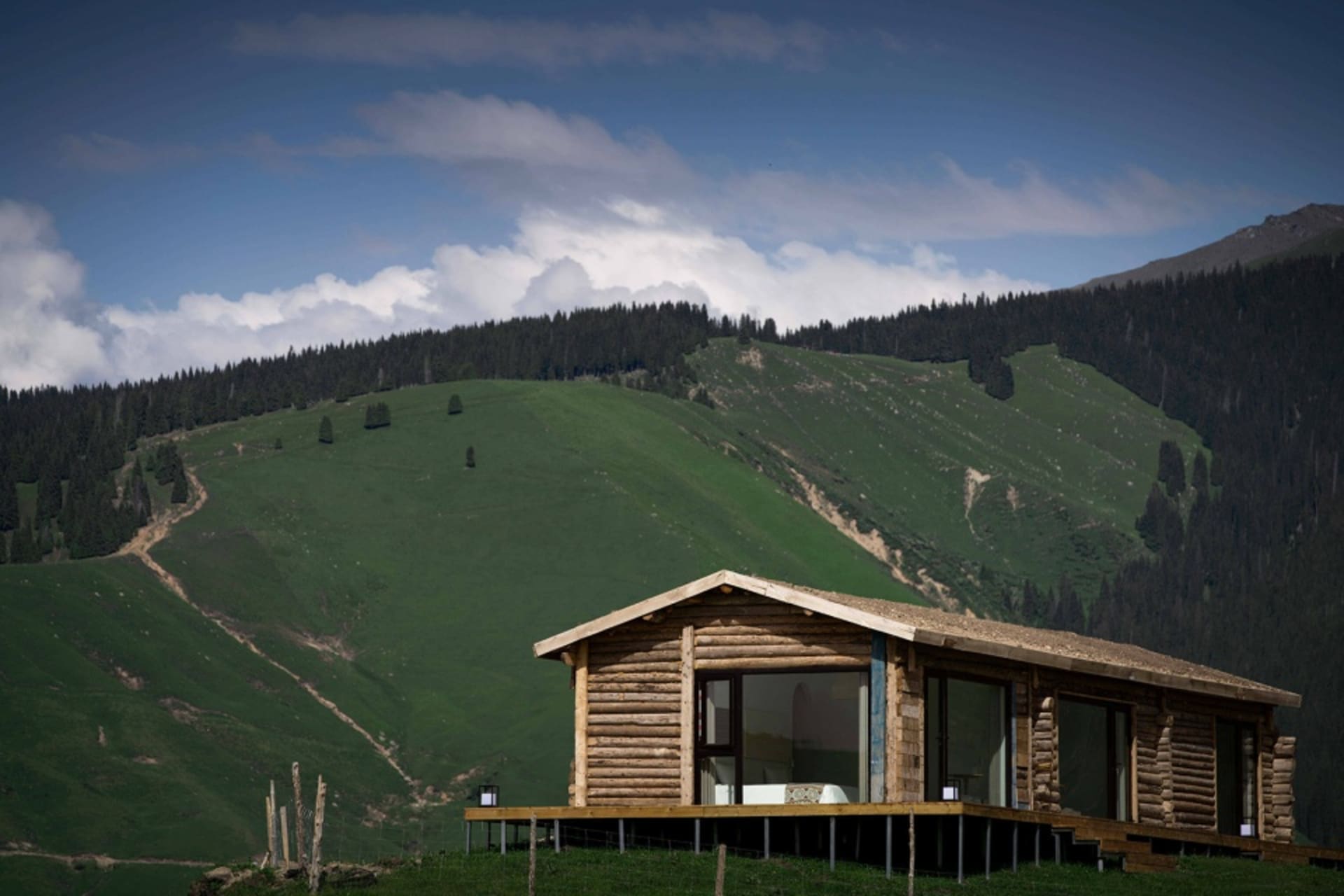 A cozy, rustic living room with wooden furniture and a large window overlooking green hills.