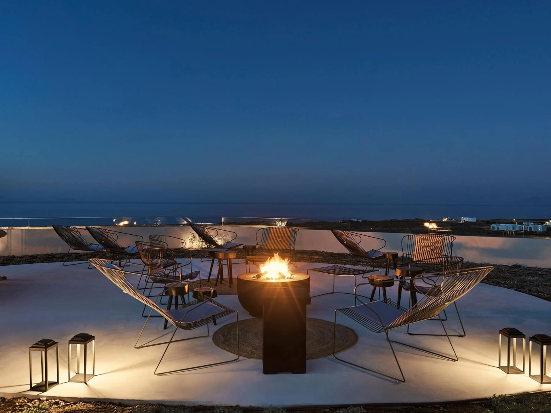 Industrial-style outdoor lounge with metal chairs and a fire pit at night.