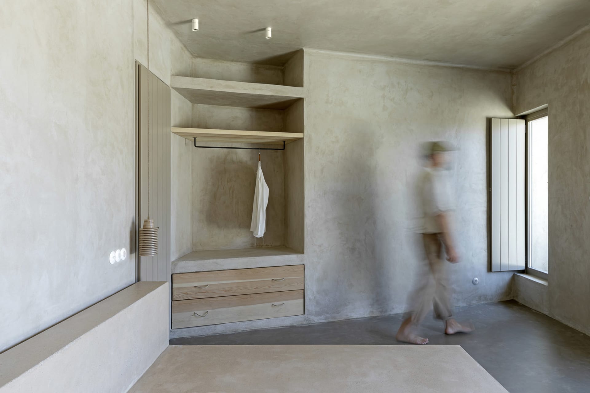 A minimalist concrete wardrobe with a white shirt hanging on a clothes rail.
