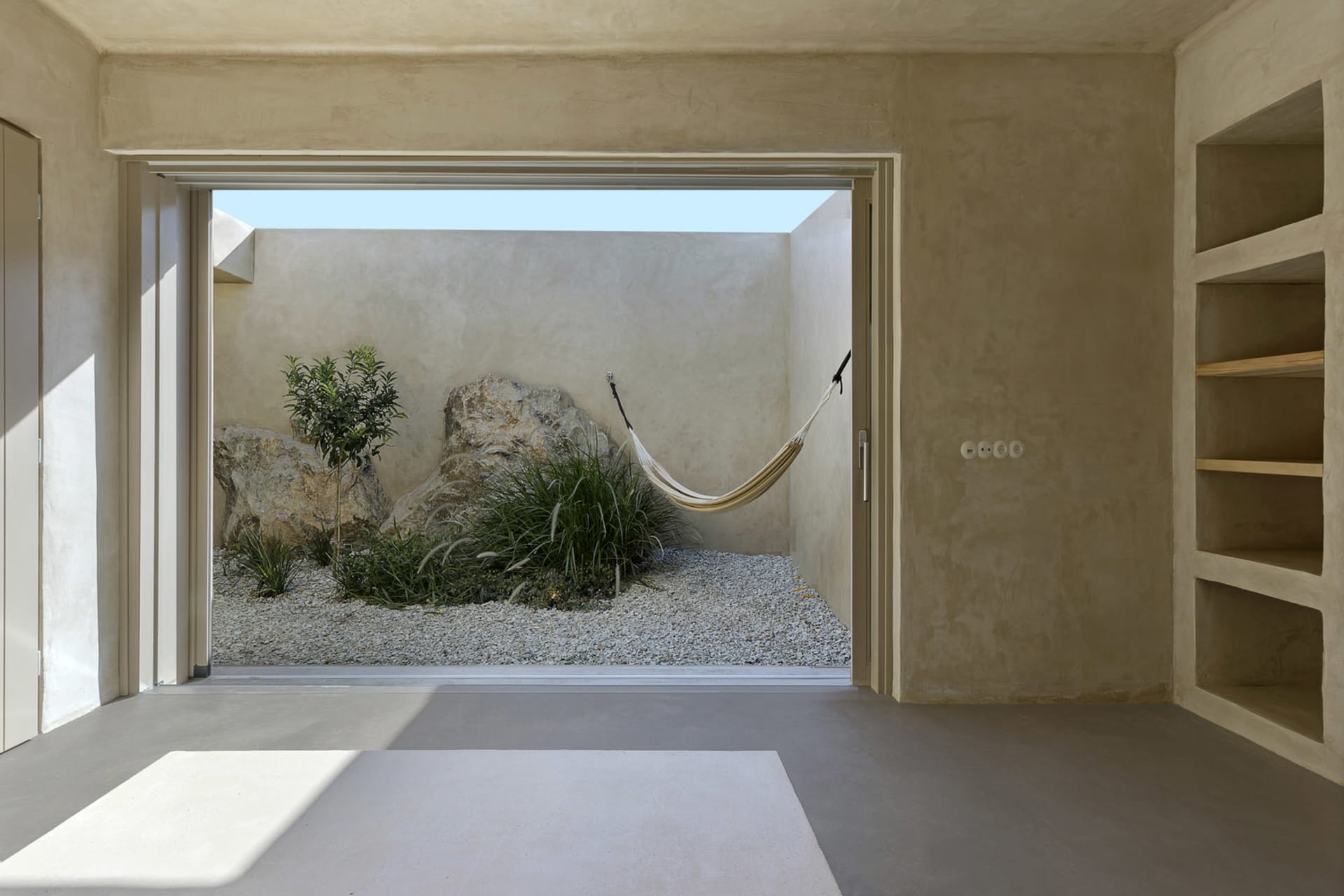 Minimalist-style indoor garden with concrete walls, rocks, and a hammock.
