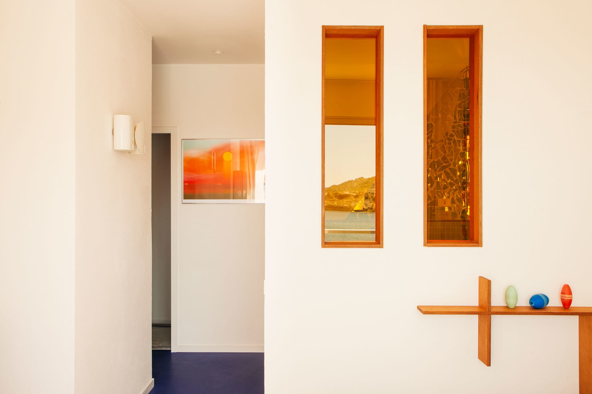Modern hallway with white walls, ceiling and floor, windows, artwork, and sculptures.