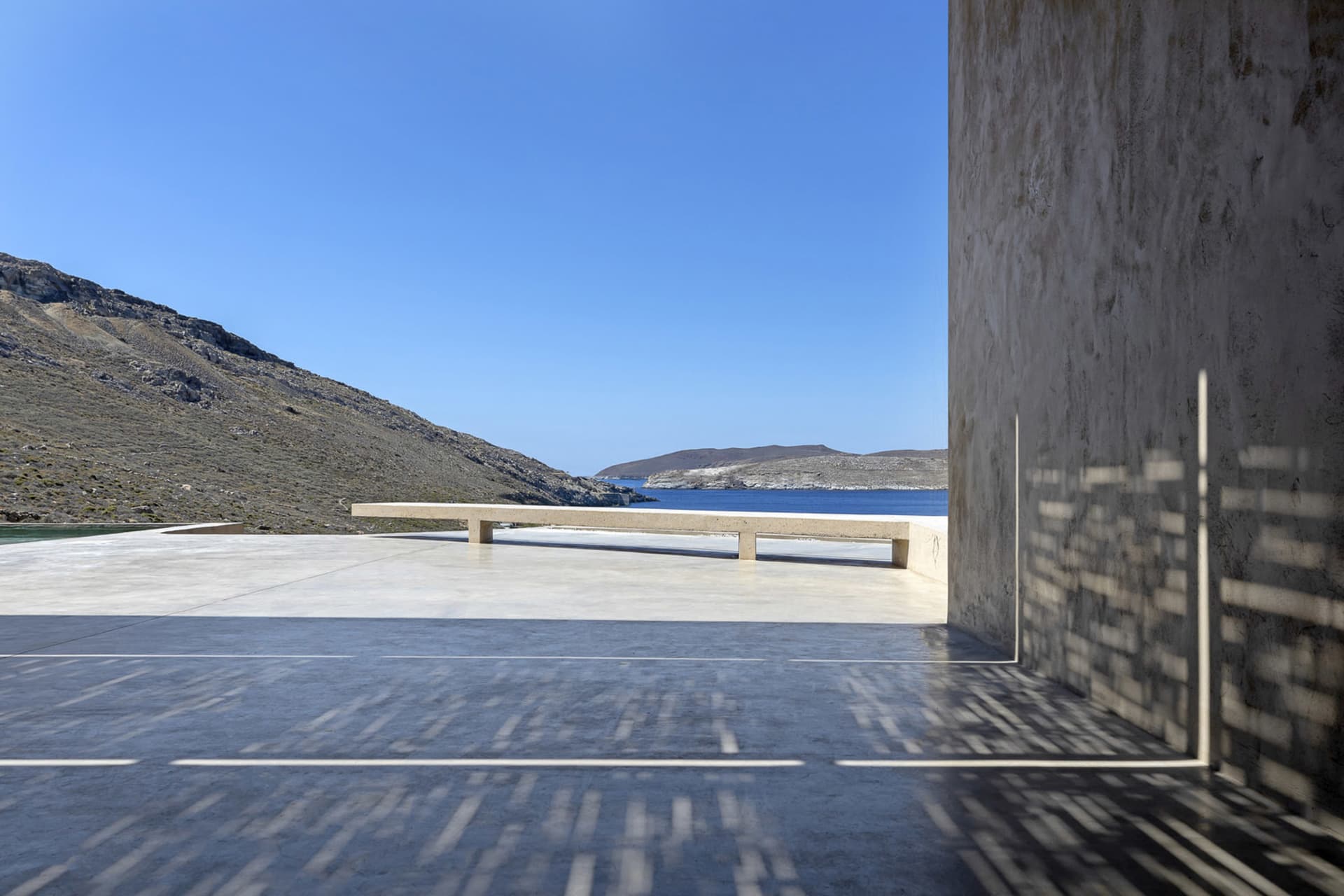 A modern minimalist landscape featuring concrete and stone surfaces with expansive views of a serene coastal area and distant