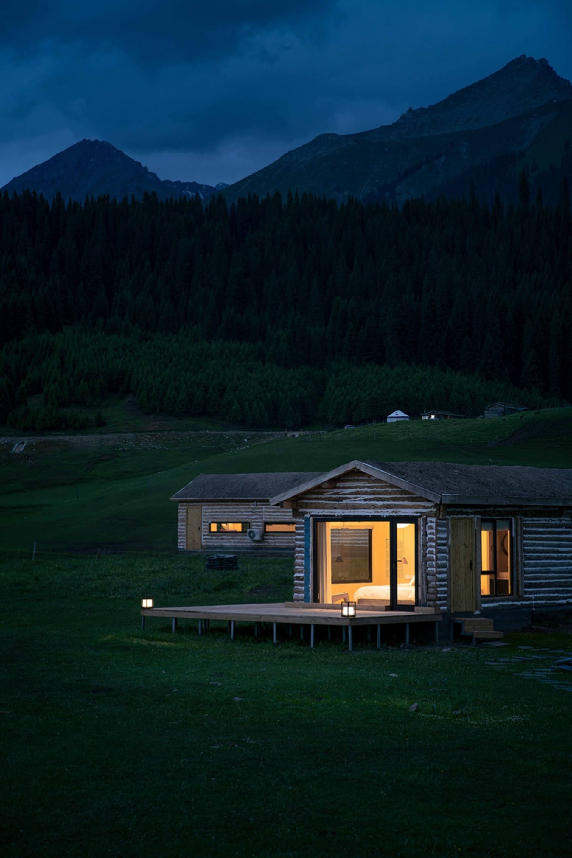 A cozy camping cabin with a wooden exterior and warm indoor lighting in a mountainous setting.