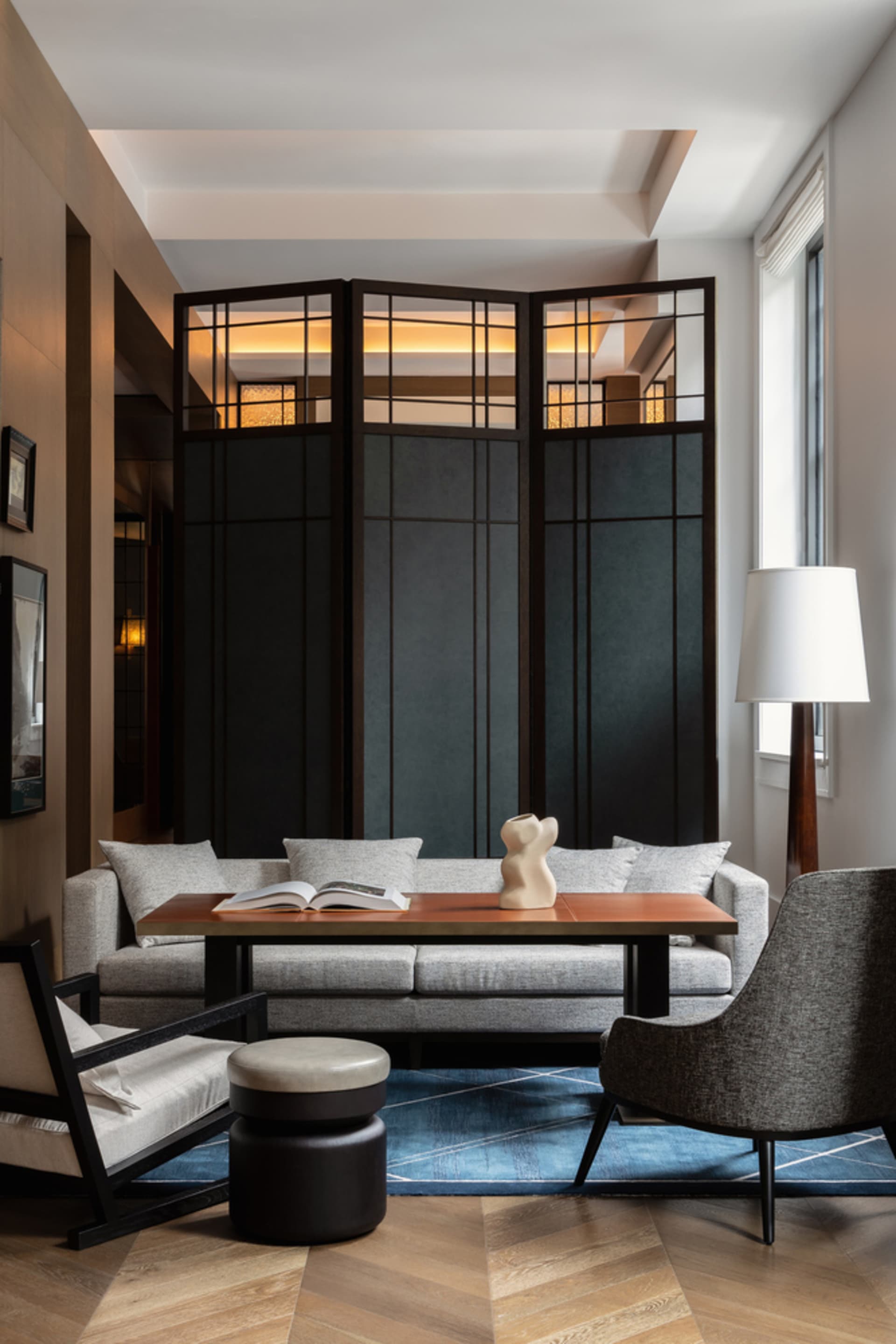 A minimalist living room with wood tiles, a fabric couch, and a glass panel room divider.