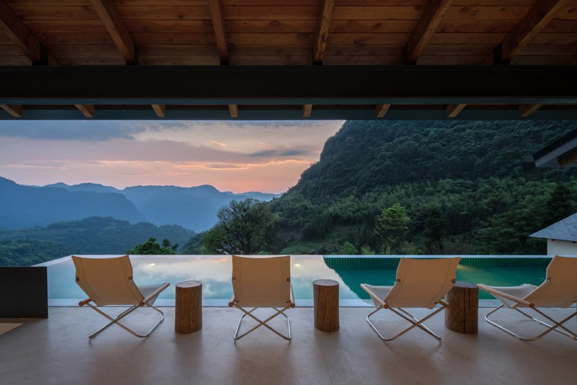 A minimalist residential deck featuring concrete flooring, steel chairs, and wooden stools.