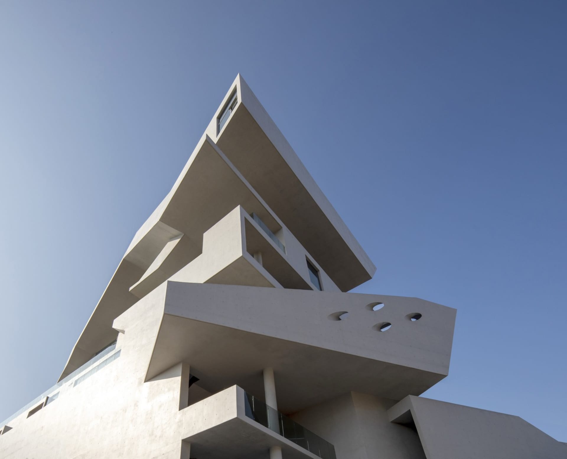 A modern architectural design featuring white concrete structures against a clear blue sky.