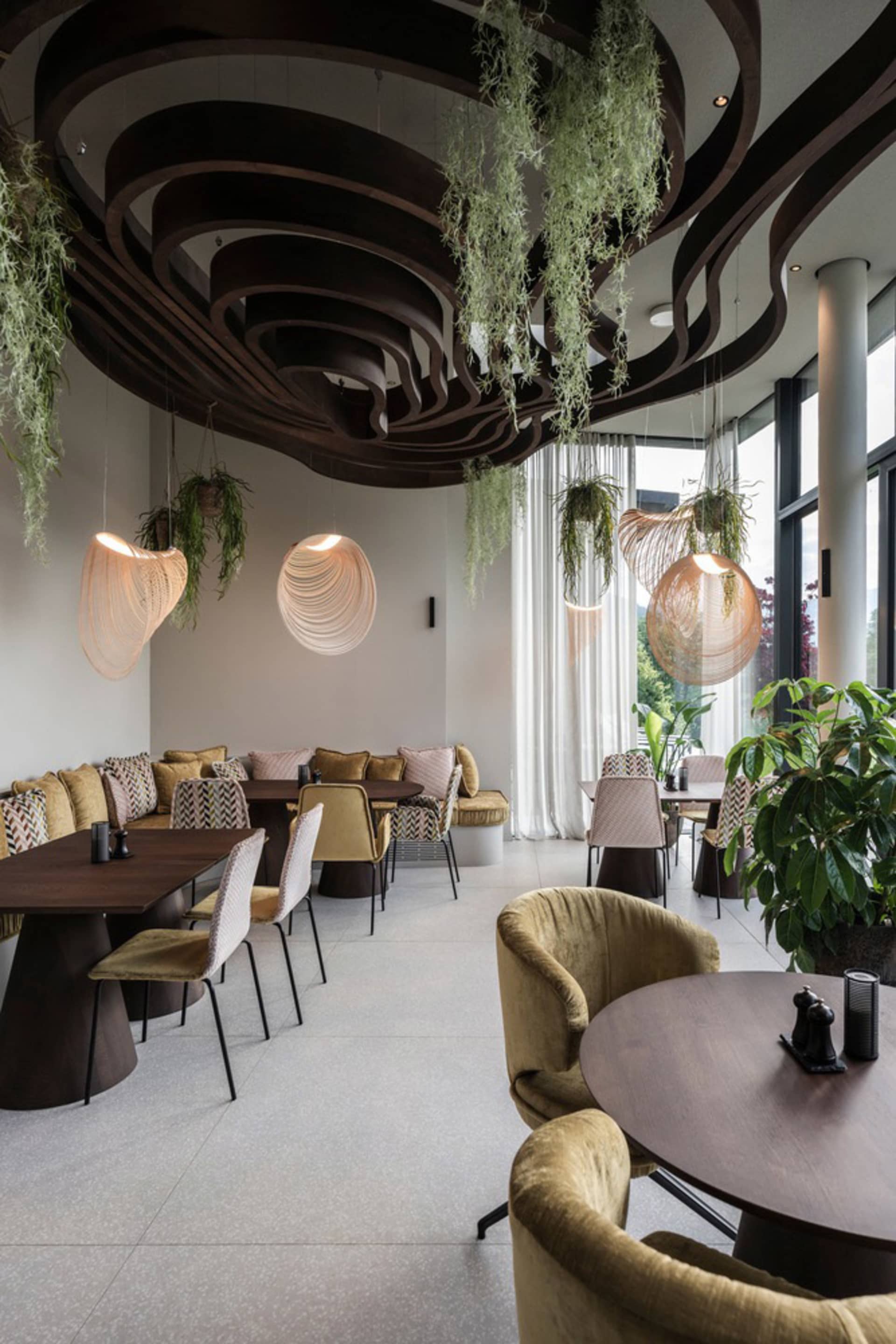 Contemporary restaurant interior featuring a wooden ceiling with circular design elements, hanging plants, and a mix of seati