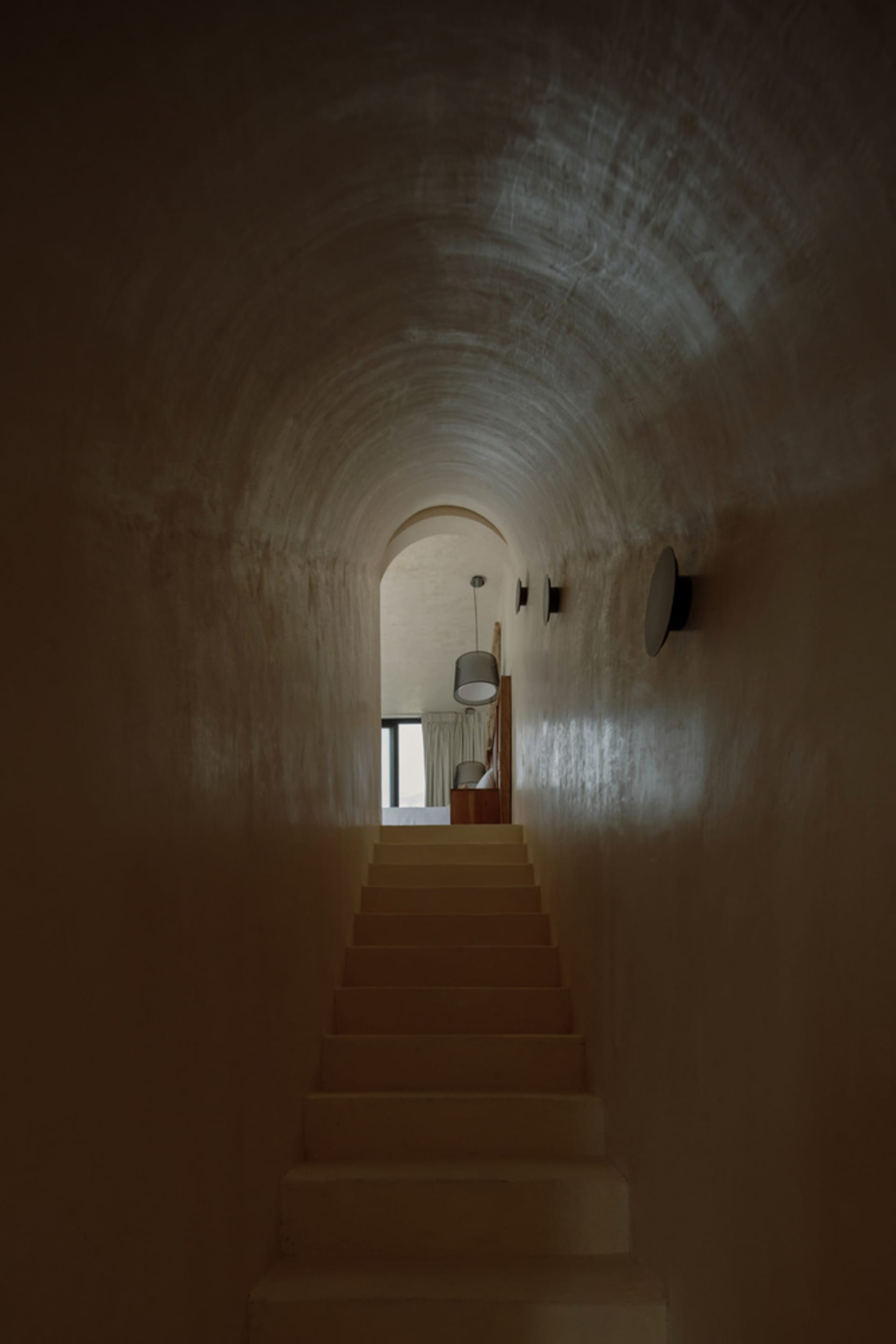 A modern staircase with smooth concrete steps, illuminated by overhead lighting, leading towards a light-filled space.