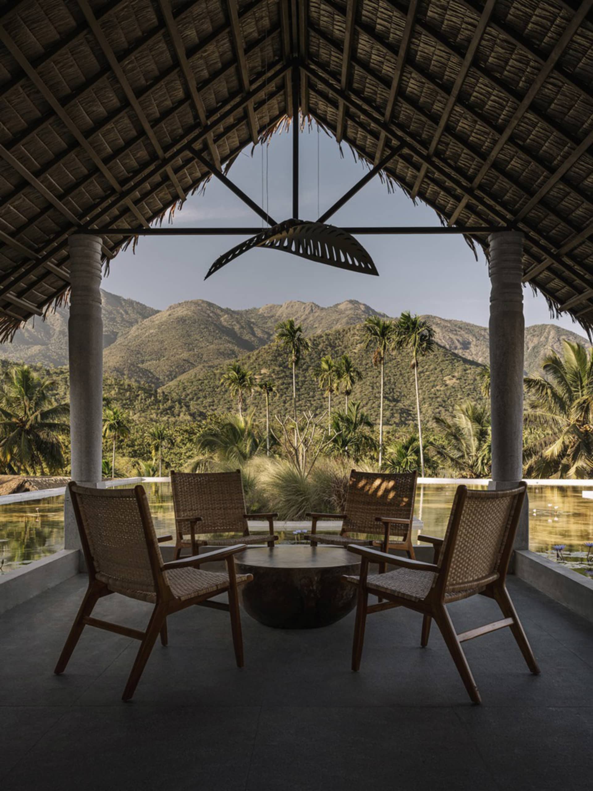 Outdoor seating area with woven bamboo furniture overlooking mountains and palm trees.