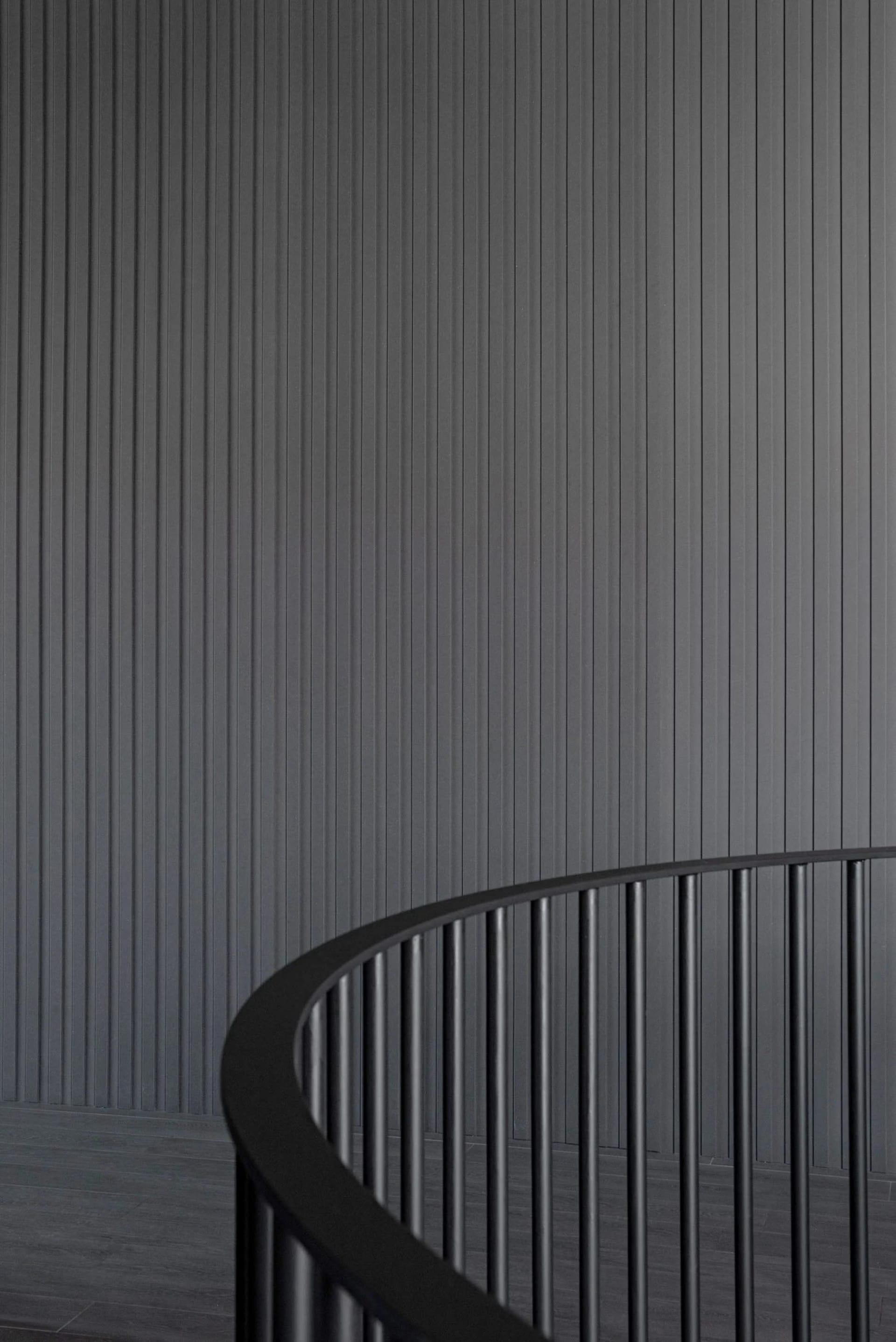 A modern minimalist staircase with a black metallic railing against a dark textured wall.