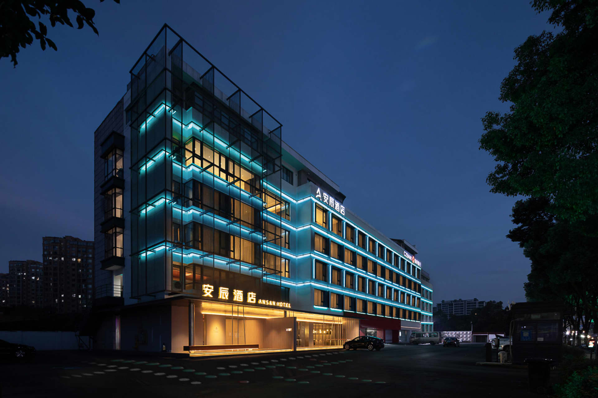 A modern hotel exterior featuring glass walls and illuminated by LED lighting at dusk.