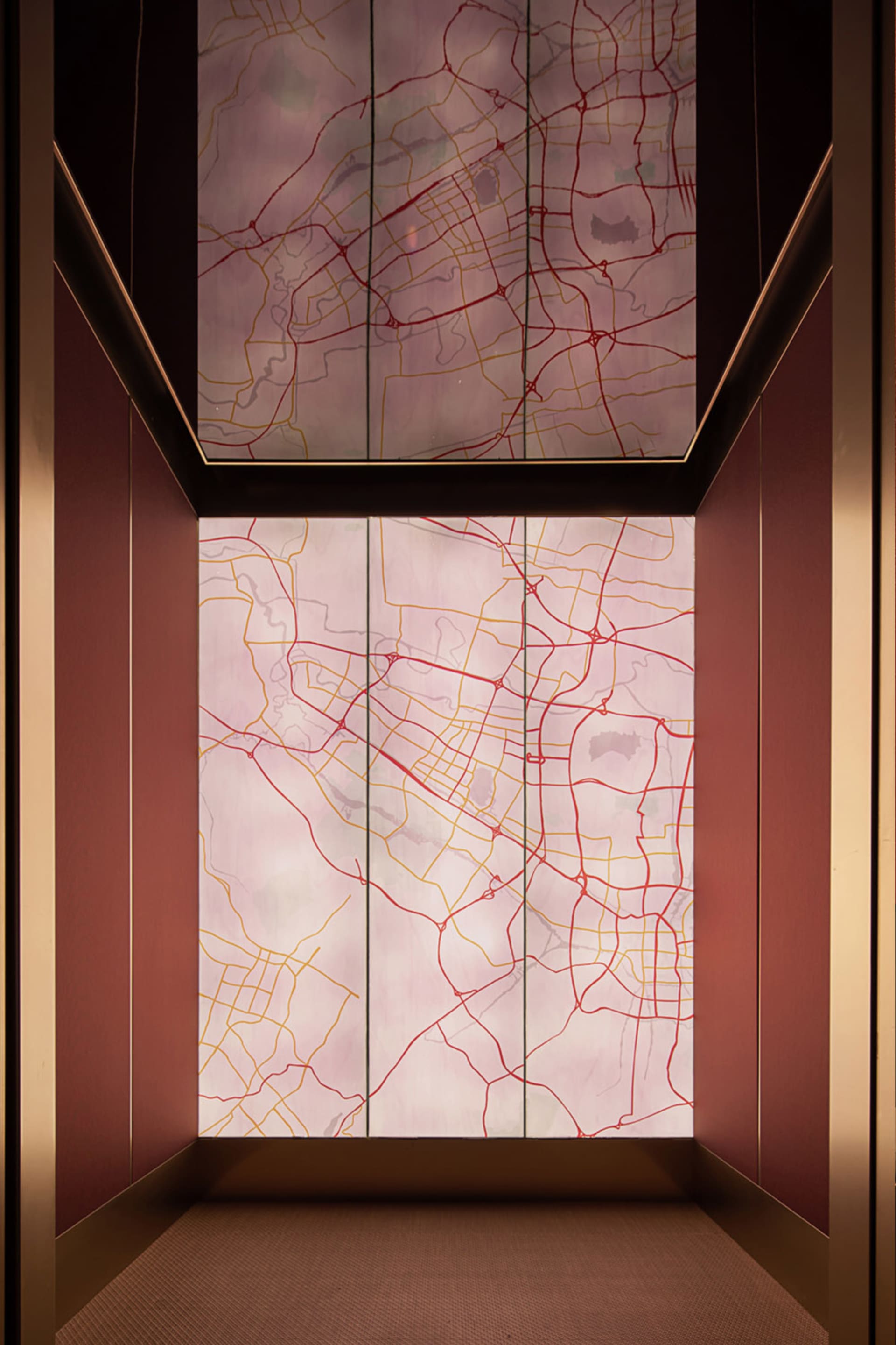 A modern lobby interior featuring a glass wall displaying a map with red and yellow lines and patterns.