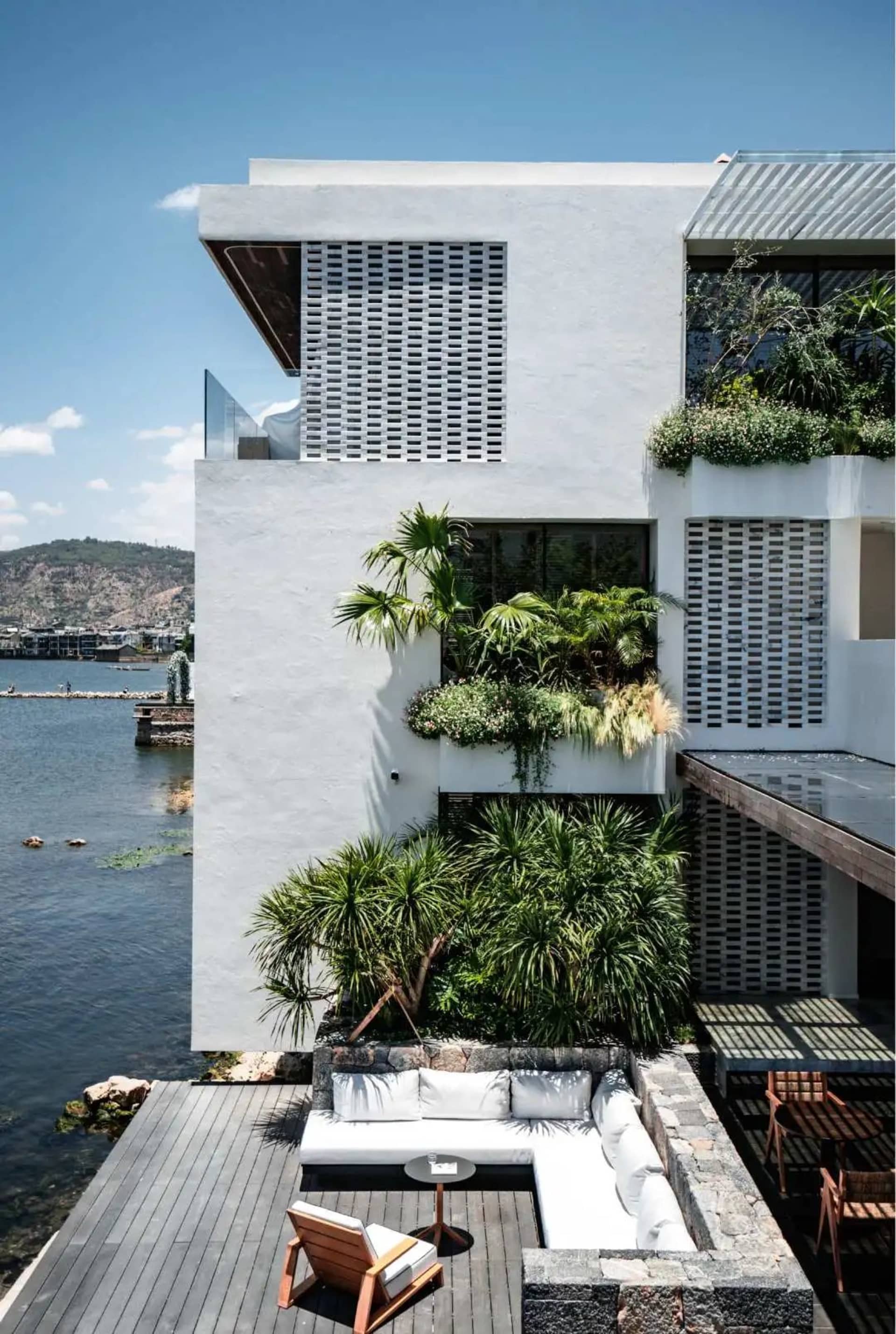 Modern residential exterior with minimalist design, featuring concrete and glass elements, surrounded by water.