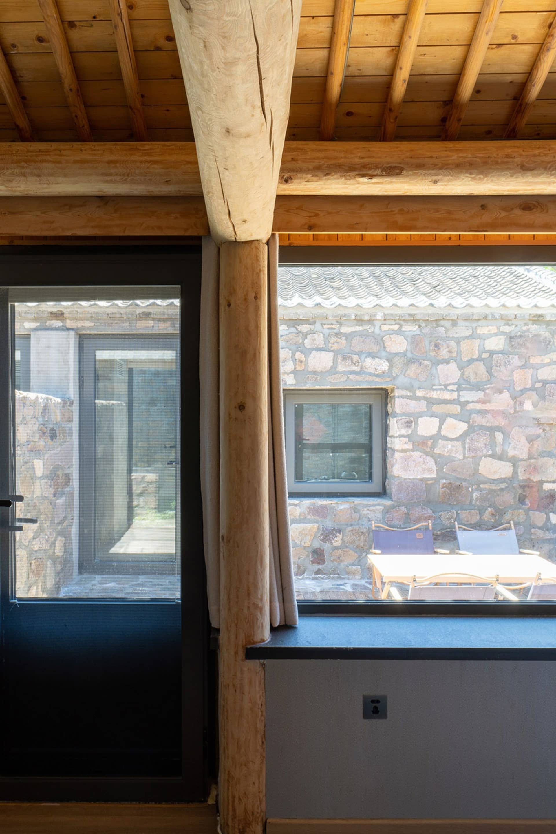 A rustic kitchen with stone walls, wooden beams, and glass windows.
