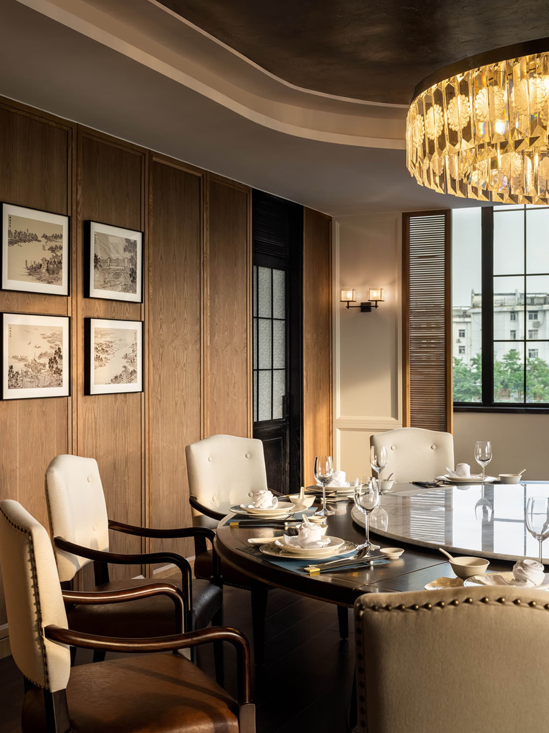 An elegant dining room with modern glass furniture, a round table, and white upholstered chairs.