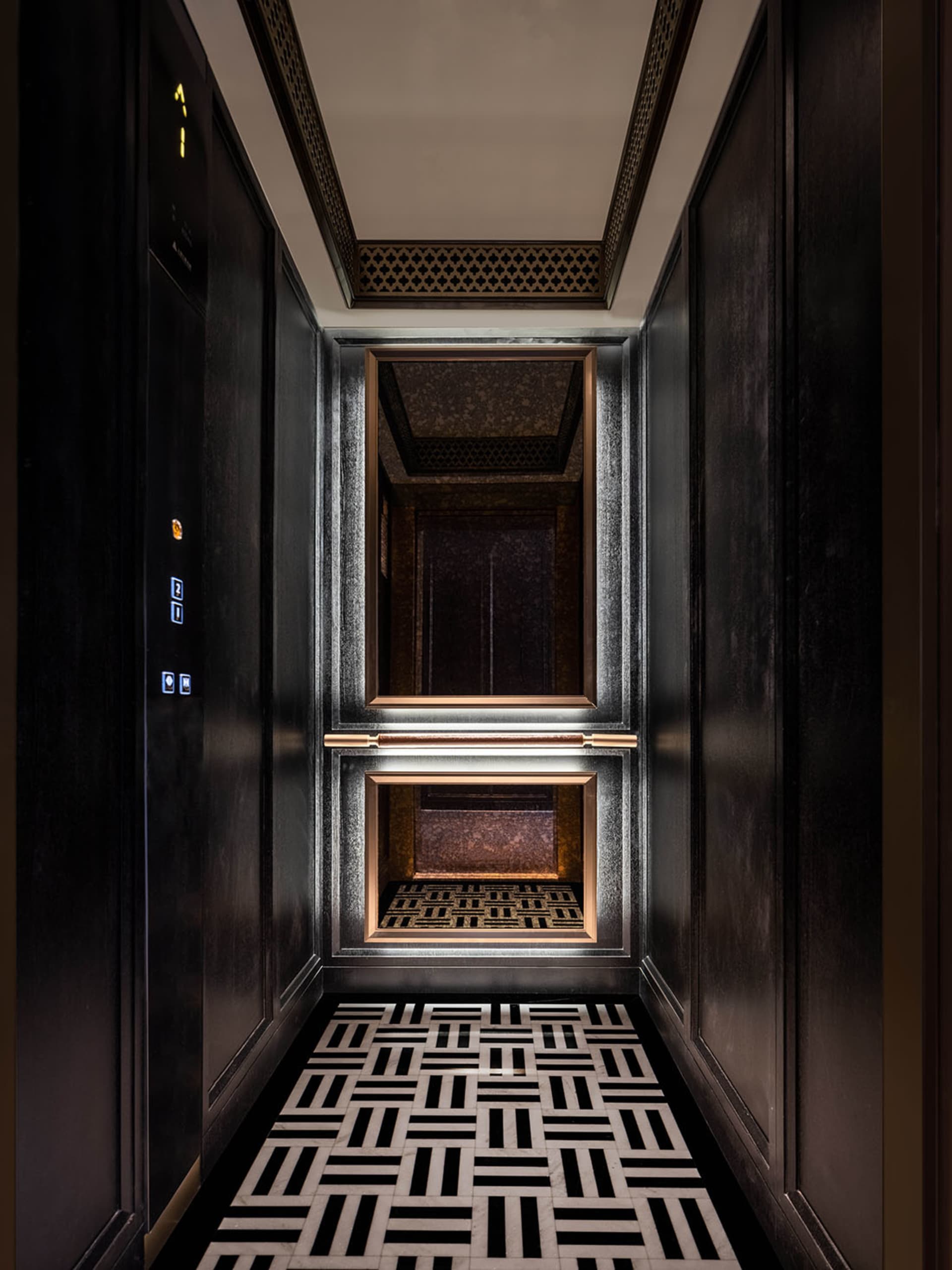 Modern elevator interior with black and white flooring, metallic accents, and geometric design.