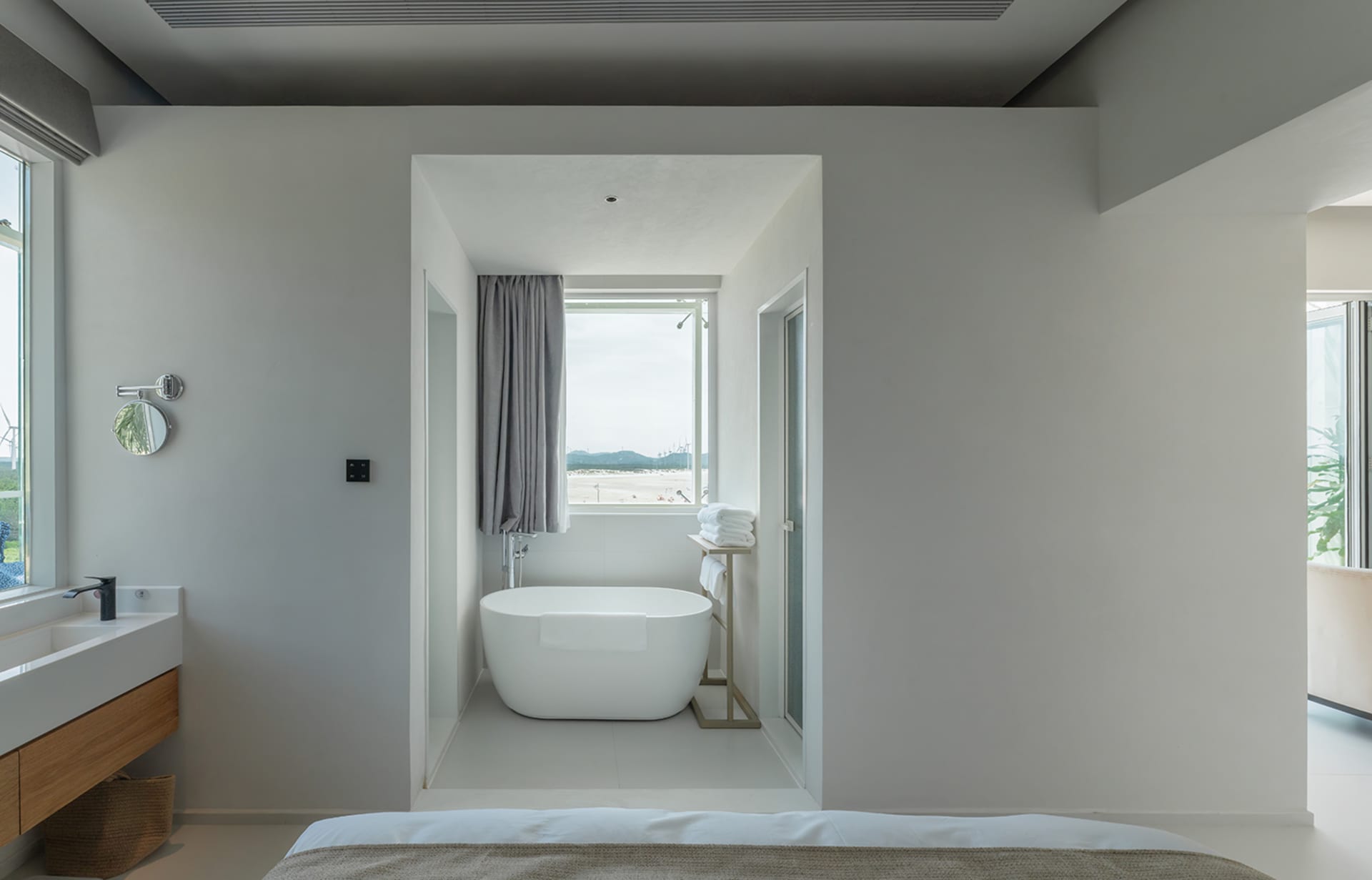 Modern minimalist bedroom featuring a white wall and a white bathtub with a window overlooking the beach.