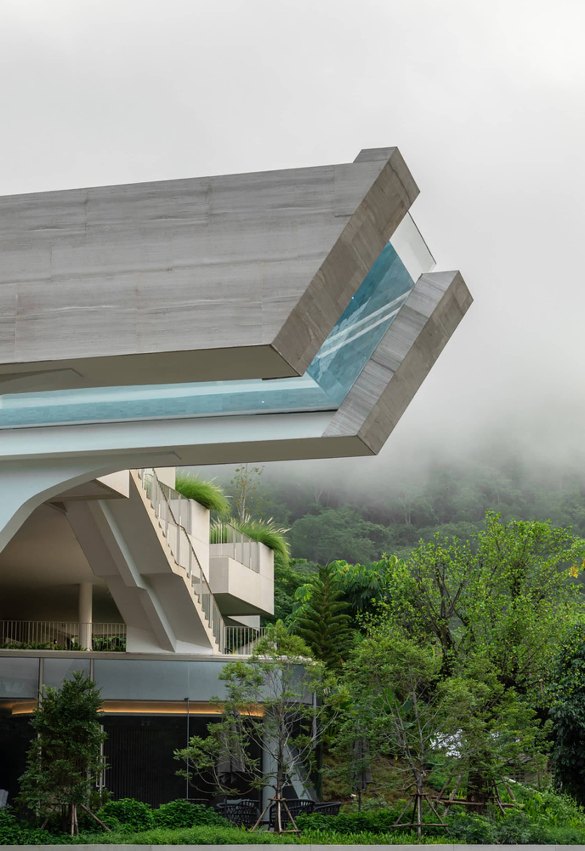 A modern architectural structure with a unique concrete design, featuring a cantilevered window and lush greenery.