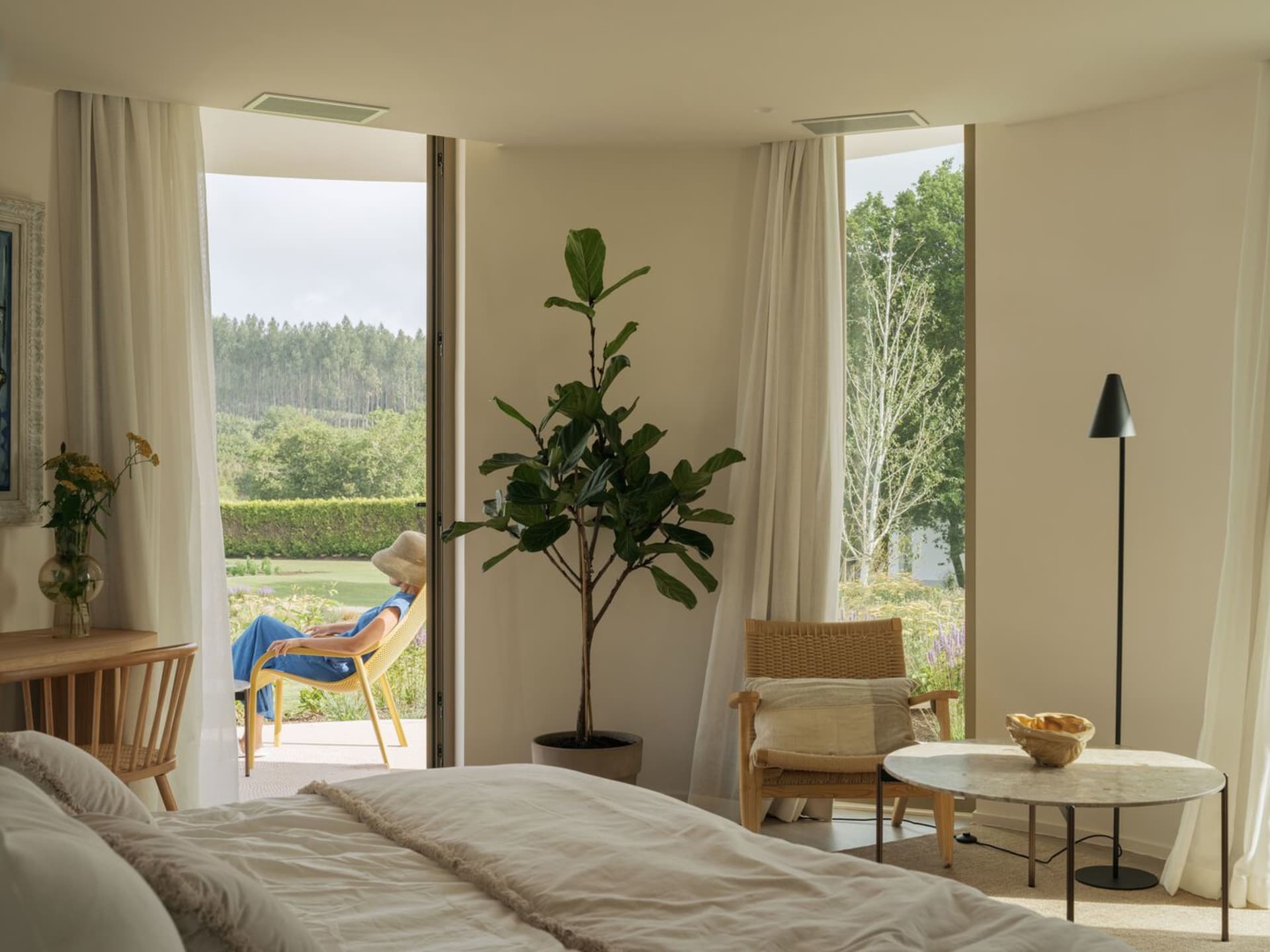 A modern bedroom featuring a cozy bed with white bedding, a wooden floor, and minimalist furniture.