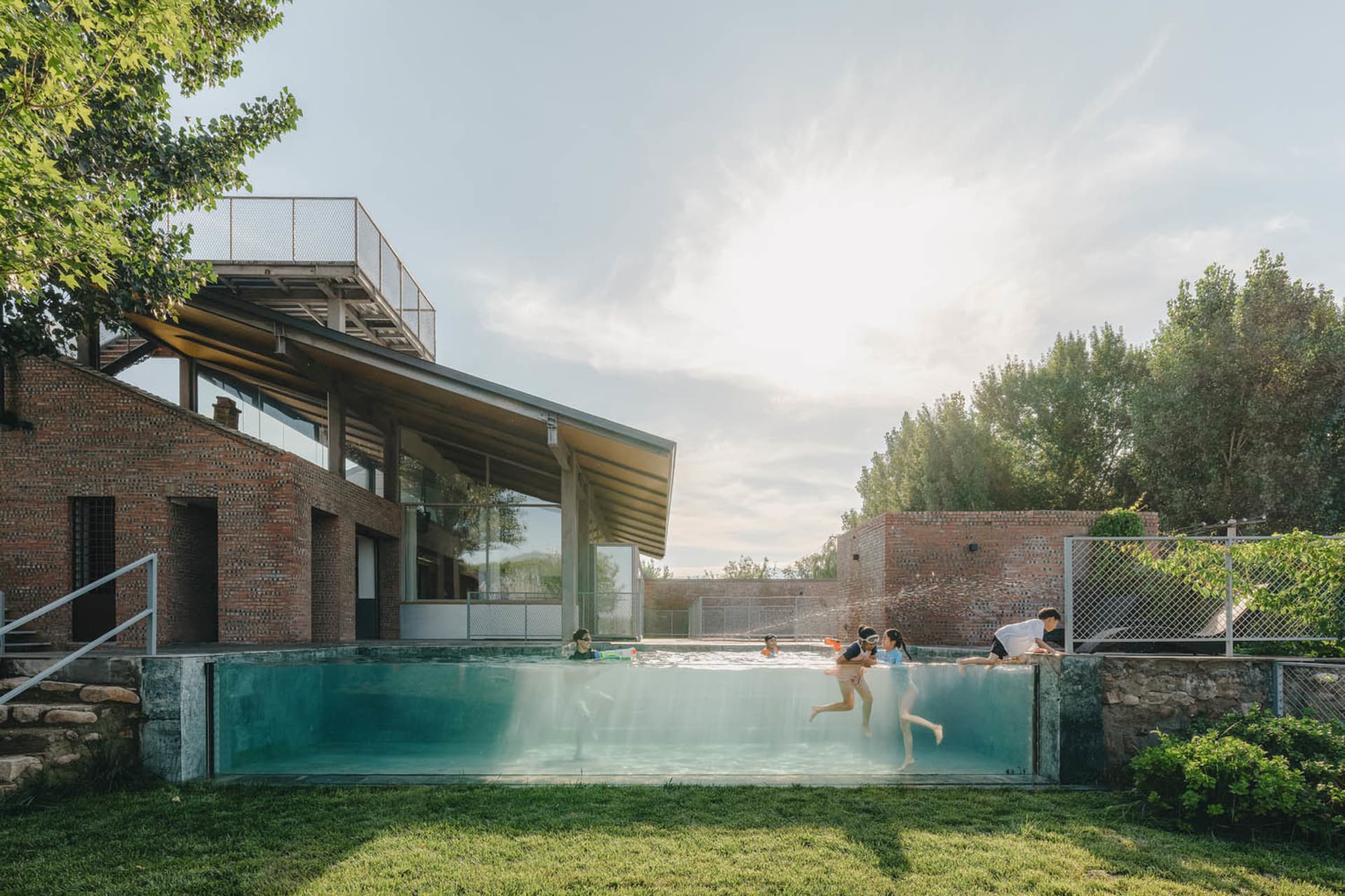 People enjoying a modern glass swimming pool in a residential outdoor area with concrete structures.