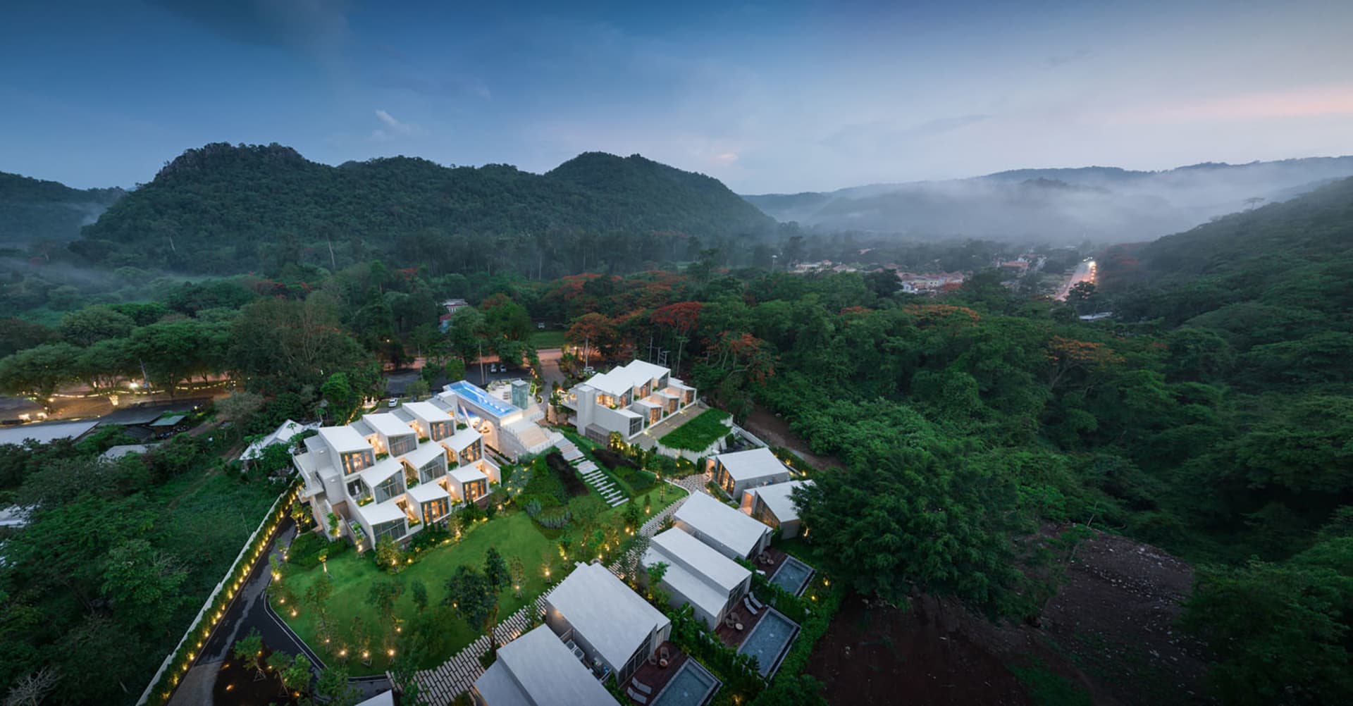 Aerial view of a modern residential property nestled in a lush, green landscape with mountains in the background.
