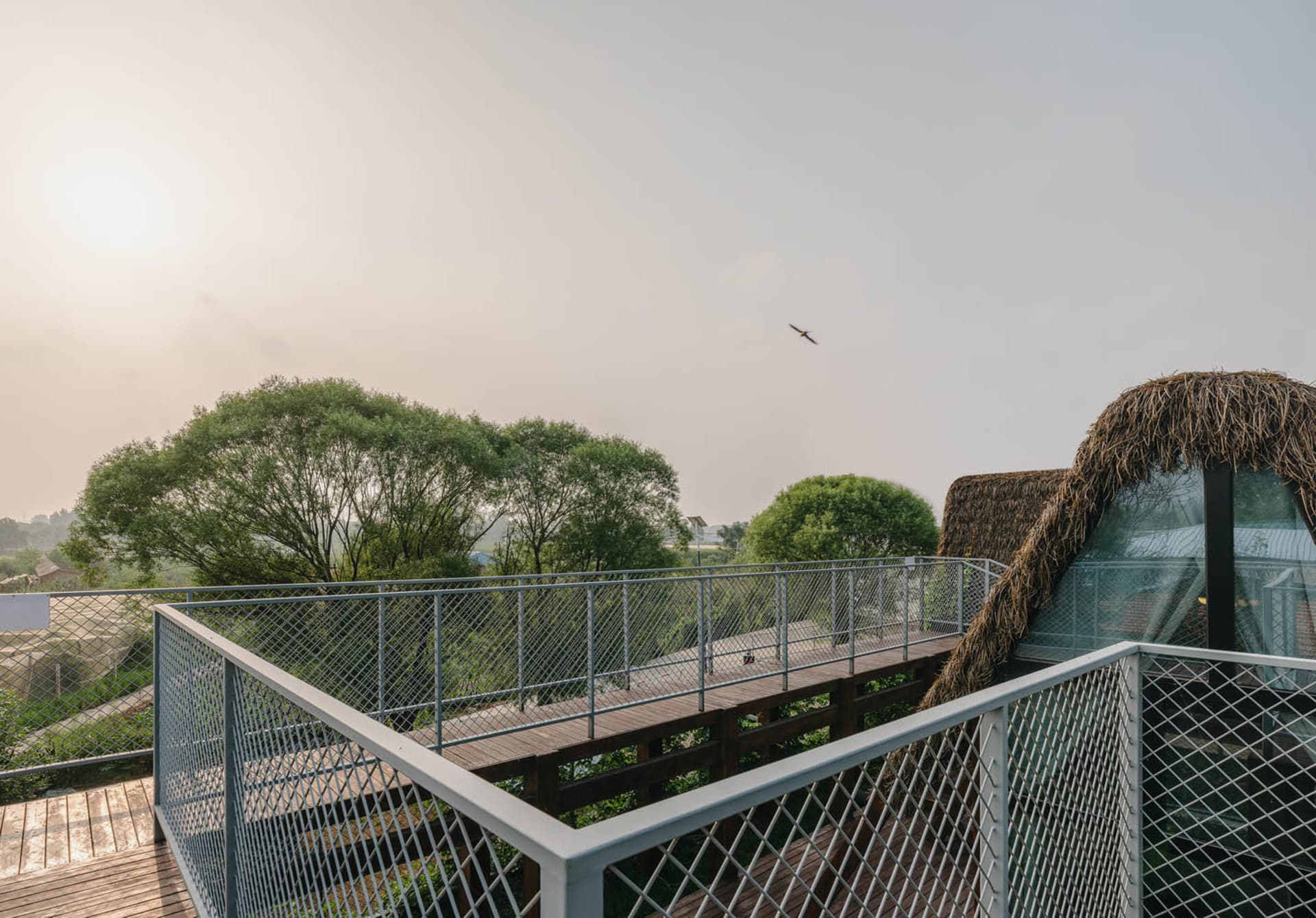 A deck with a thatched roof and metal railing overlooking a tree-lined area.
