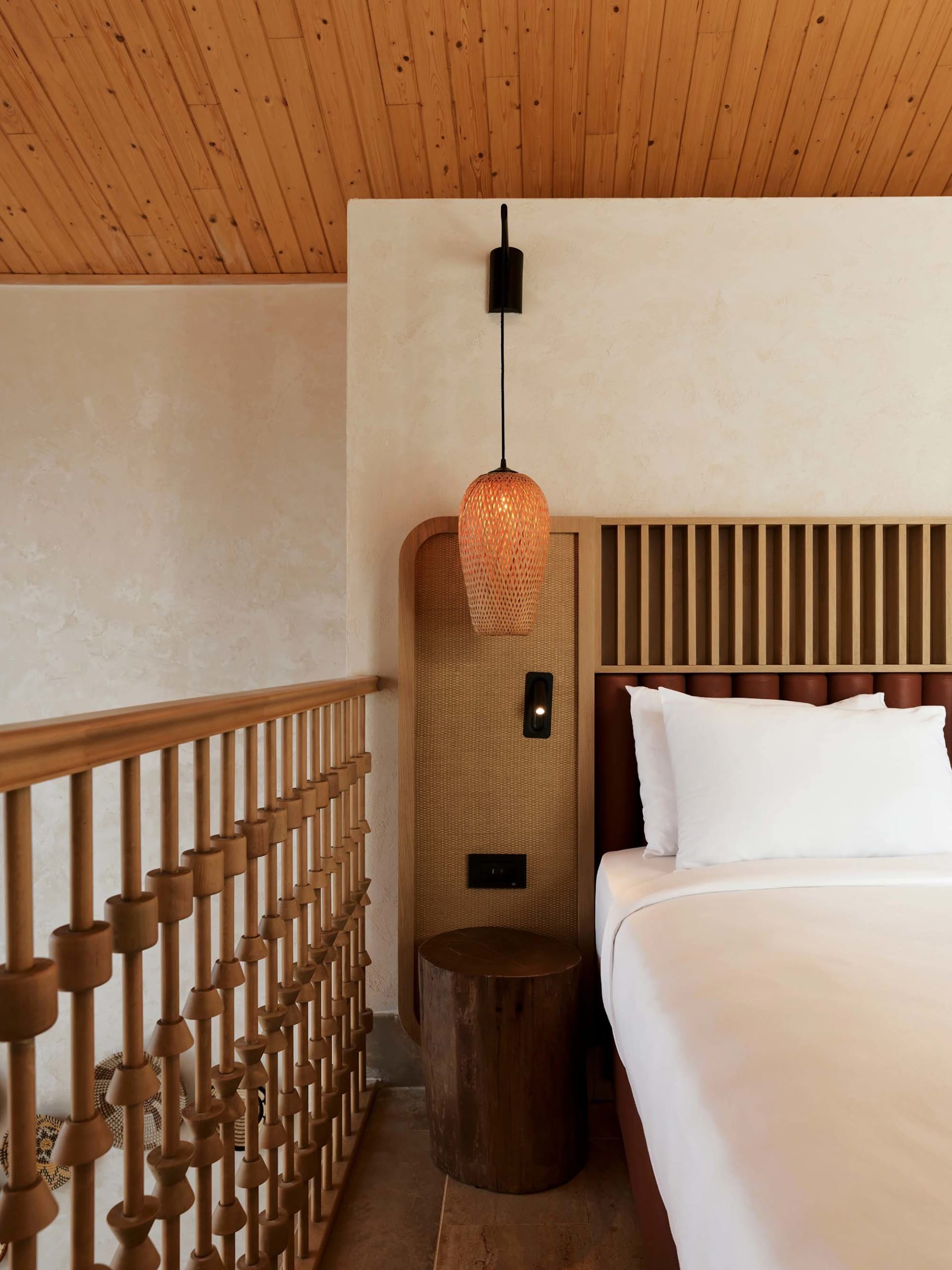 Minimalist bedroom featuring a wooden bed with a wooden headboard and a wooden bedside table with a woven pendant lamp.