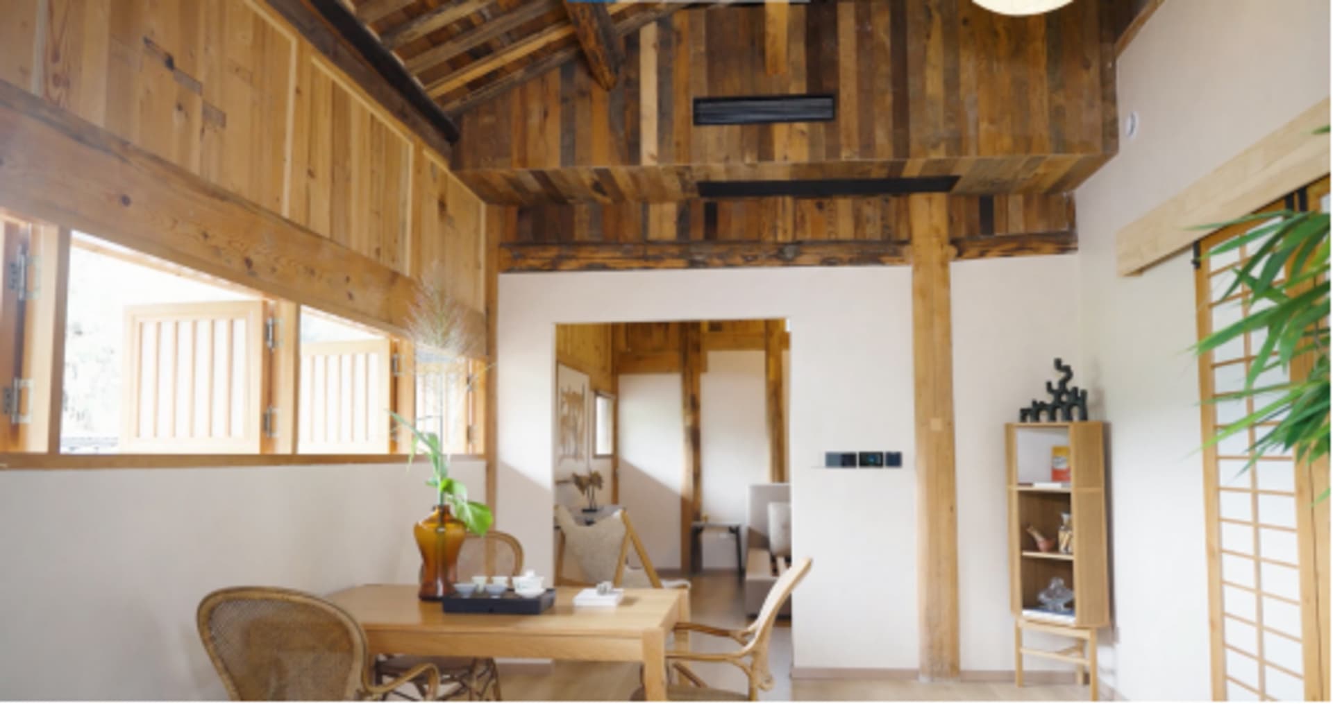 A minimalist living room with wooden furniture and walls, featuring a tea table and chairs.