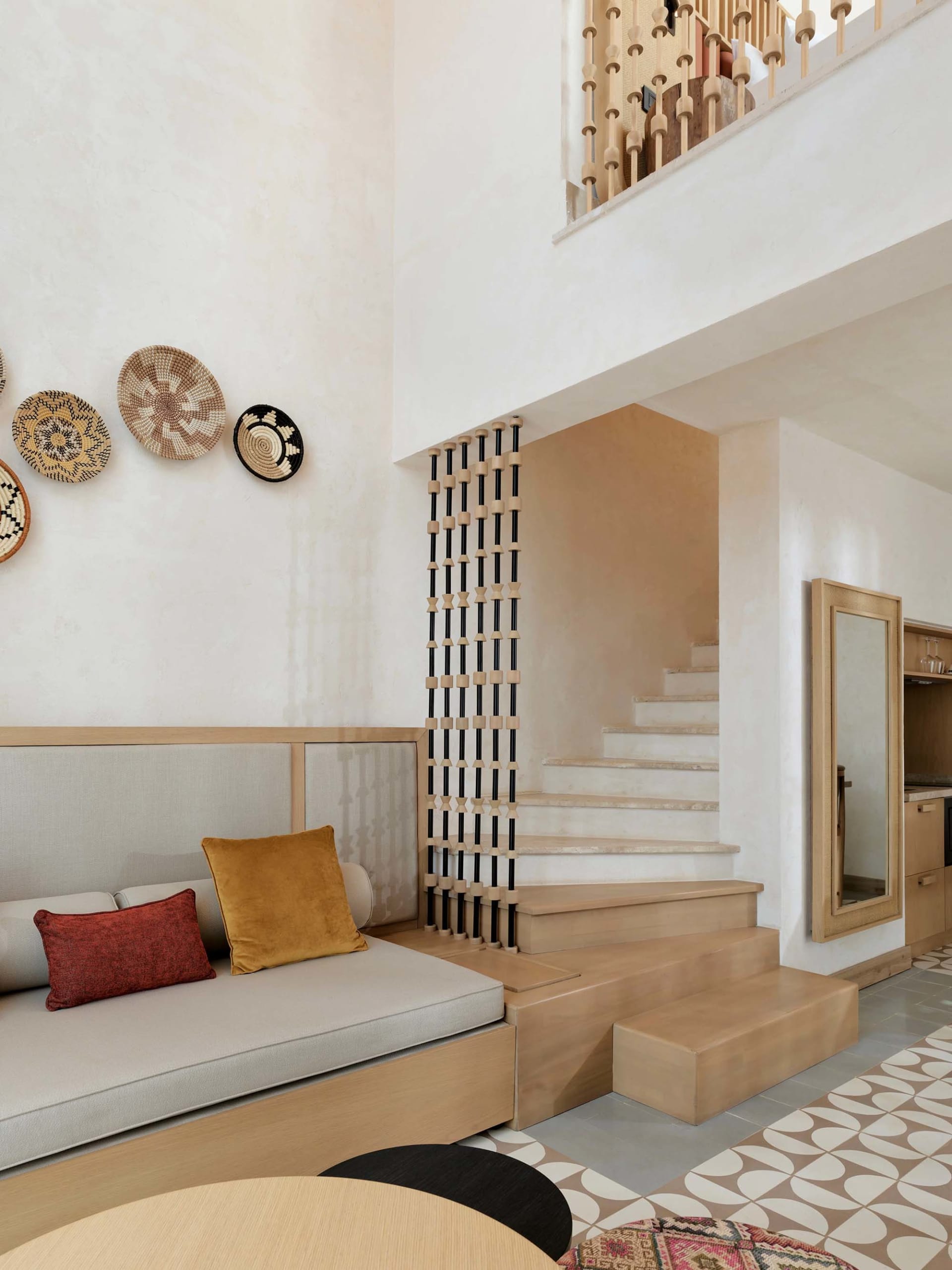 A modern living room featuring a concrete wall, patterned floor tiles, and a wooden sofa with yellow and red pillows.