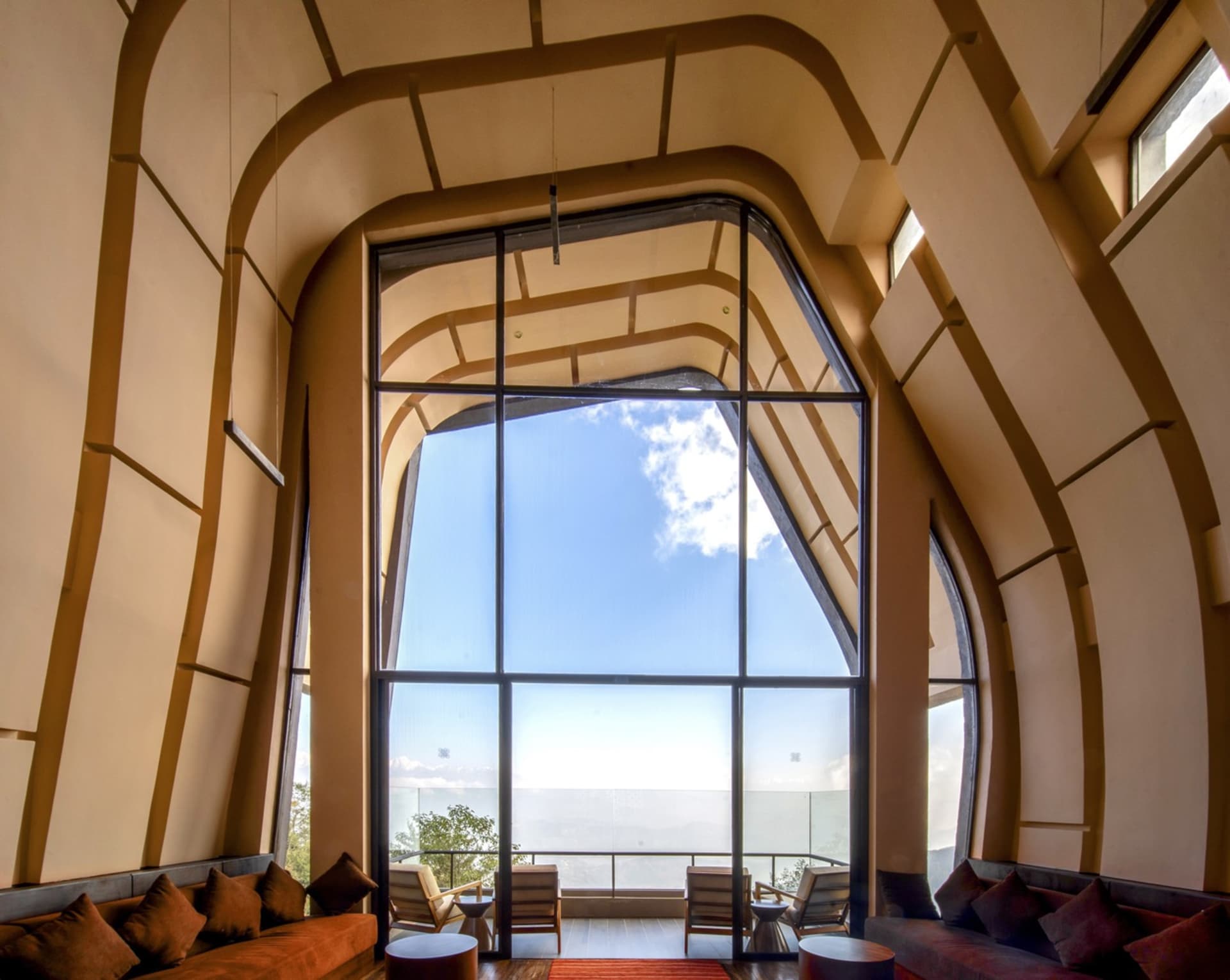 A modern living room with a large glass window showing a clear blue sky and distant views.