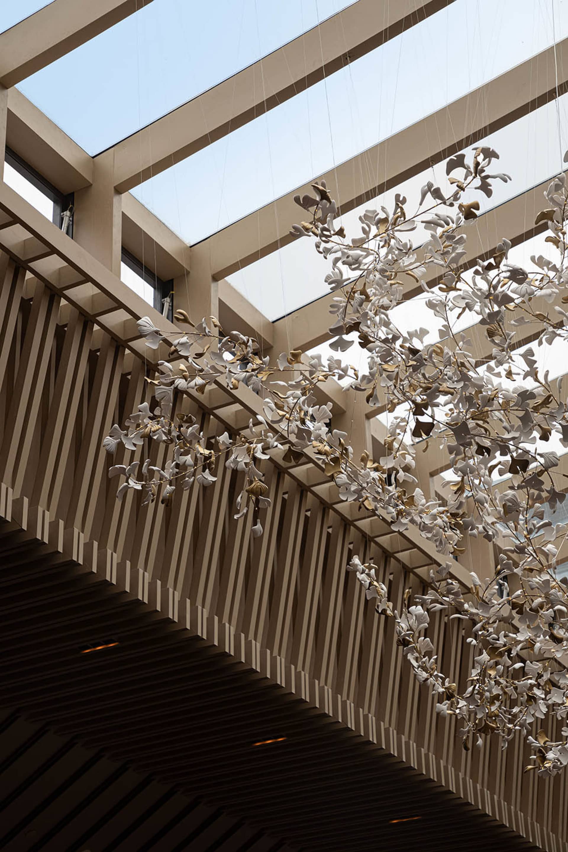 Ceramic branches hanging from a modern architectural space with skylights.